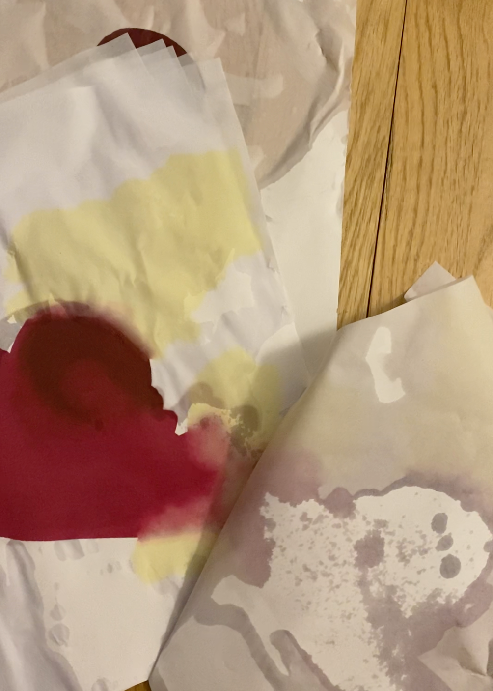 Three water stained pieces of paper reveals a yellow, dark red, and magenta abstract painting.