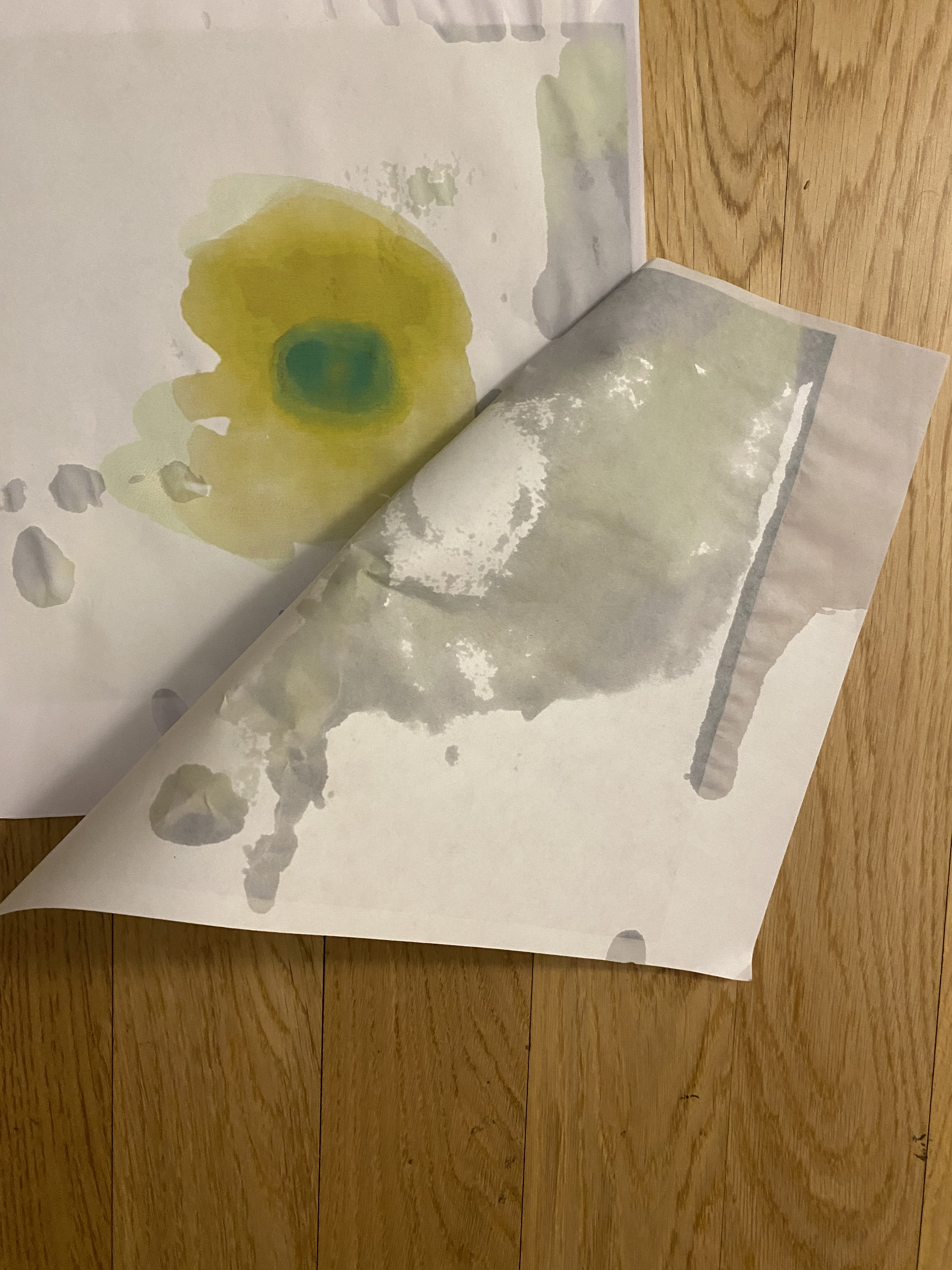 Two water stained pieces of paper is peeled back to reveal a green and yellow abstract painting.