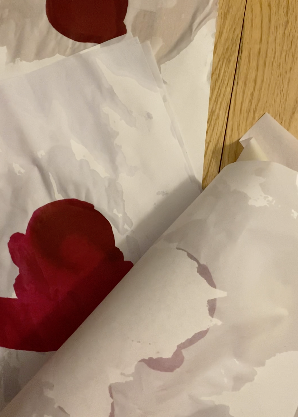 Pieces of wet paper peels back to reveal a dark red abstract painting.