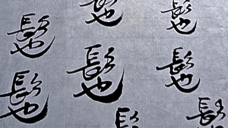 A calligraphy brush writes the words '交缠'interwoven in) on a piece of paper.