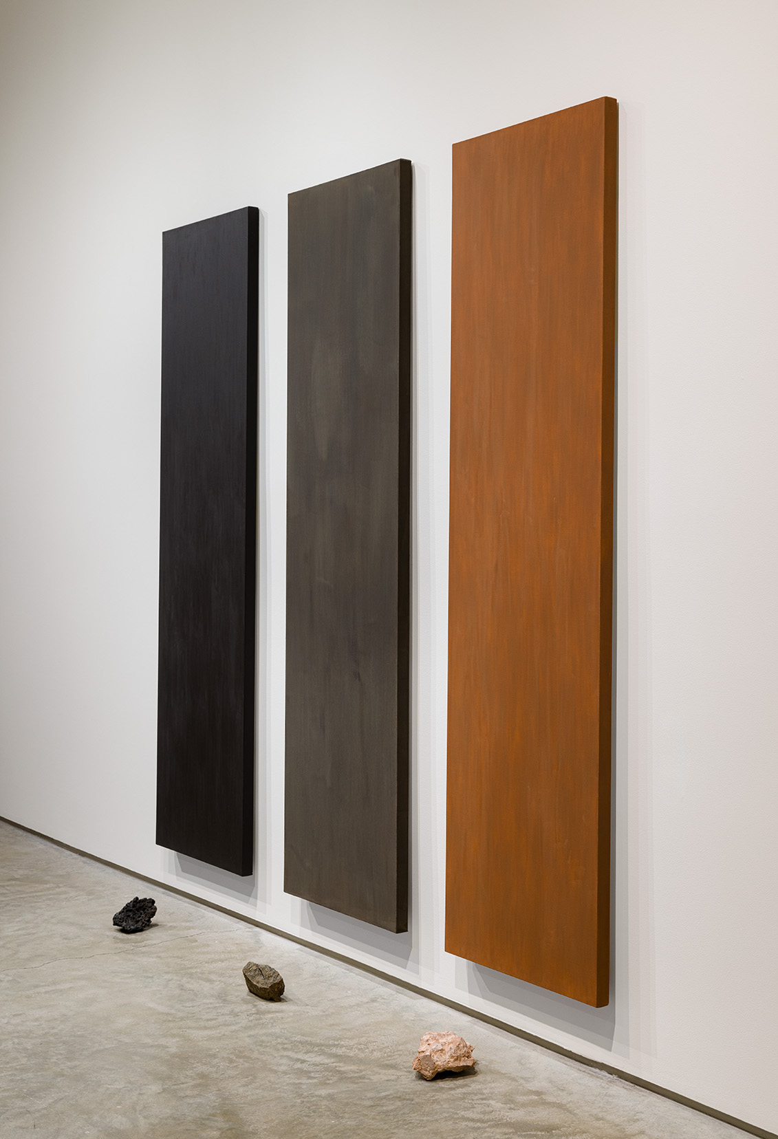 (From left to right) Michael Wang, "Mexico City," 2016. Monochrome painting made of pulverized bedrock, sample of the original rock. Painting: 70 x 19 inches, rock sample: 3 1⁄4 x 5 1/16 x 3 5/16 inches; "Marrakech," 2015. Monochrome painting made of pulverized bedrock, sample of the original rock. Painting: 70 x 19 inches, rock sample: 3 x 6 1/8 x 4 1/16 inches; "Santiago," 2017. Monochrome painting made of pulverized bedrock, sample of the original rock. Painting: 70 x 19 inches, rock sample: 2 7/8 x 6 1/4 x 3 3/16 inches. Photo by Etienne Frossard.