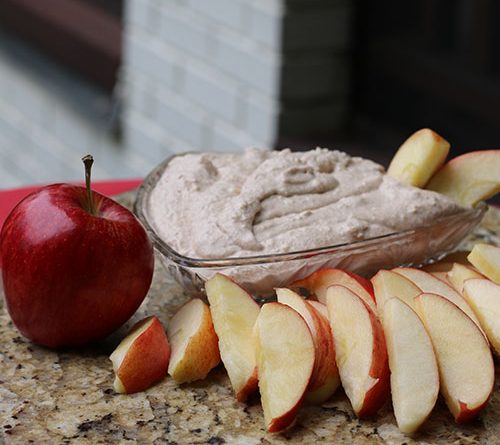 Picture of an apple placed beside an arrangement of apple slices next to dip