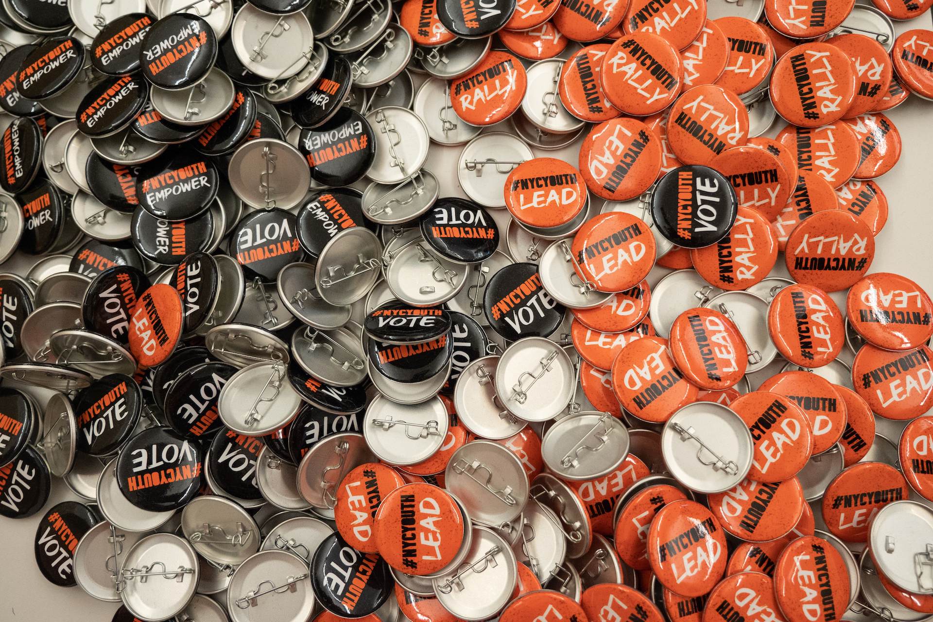 Orange and black round one inch pinback buttons designed individually with the phrases #nycyouth rally, #nycyouth lead, #nycyouth empower, and #nycyouth vote for the Democracy Corps Day of Action event.