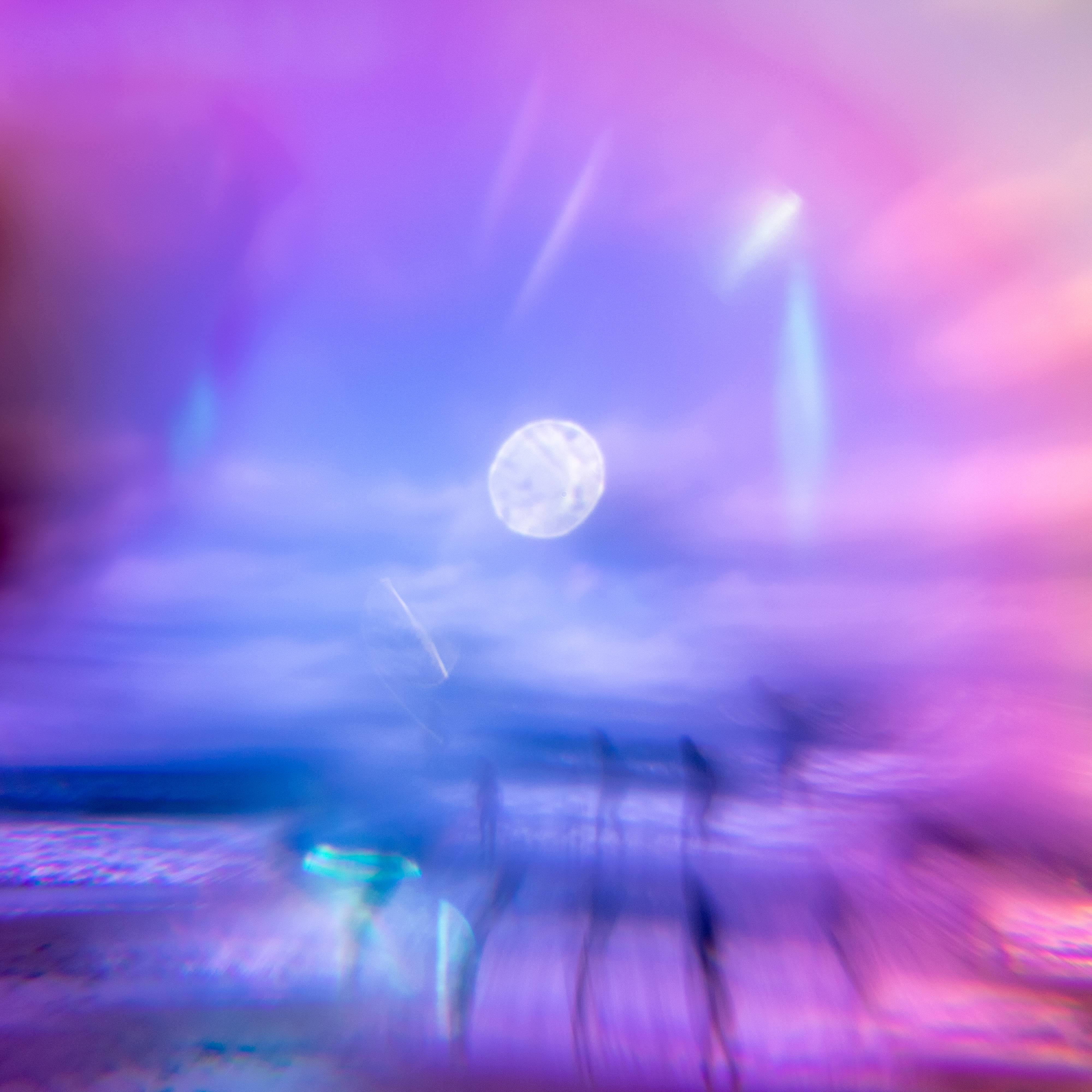 A dreamy and surreal view of a San Francisco beach is seen through a kaleidoscope, with a bright full sun in the sky. casting soft pink and purple hues over the coastal landscape.