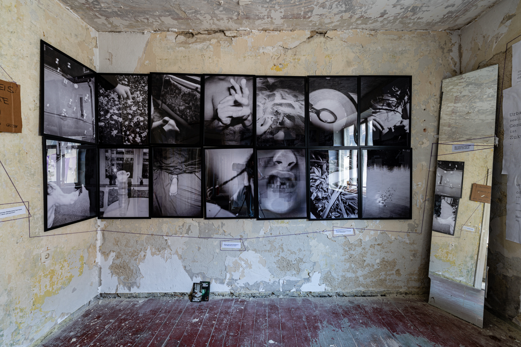 Bild 1 zu Solidarit&auml;t/care/leben:  Zwei Reihen gro&szlig;formatiger Schwarz-Wei&szlig;-Aufnahmen in schwarzen Bilderrahmen. Die Fotografien sind eng aneinander geh&auml;ngt, es sind jeweils sieben in einer Reihe. Sie zeigen allt&auml;gliche Ausschnitte. H&auml;ufig Nahaufnahmen von Kinderh&auml;nden, F&uuml;&szlig;en, einem fehlenden Milchzahn. Teilweise ist der Vordergrund des Bildes unscharf. 