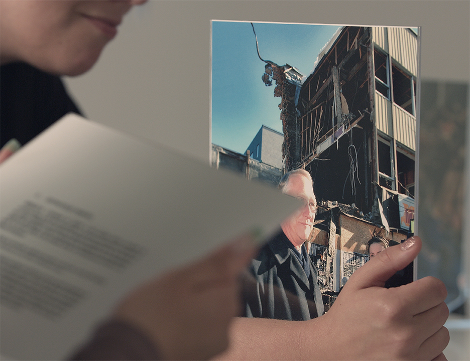 Adore tenant une photographie du maire de Montréal, Gérald Tremblay, en conférence de presse pendant la démolition du Studio XXX en 2008. Image tirée du film.Adore holding a photograph of Montreal Mayor Gérald Tremblay at a press conference during the demolition of Studio XXX in 2008.