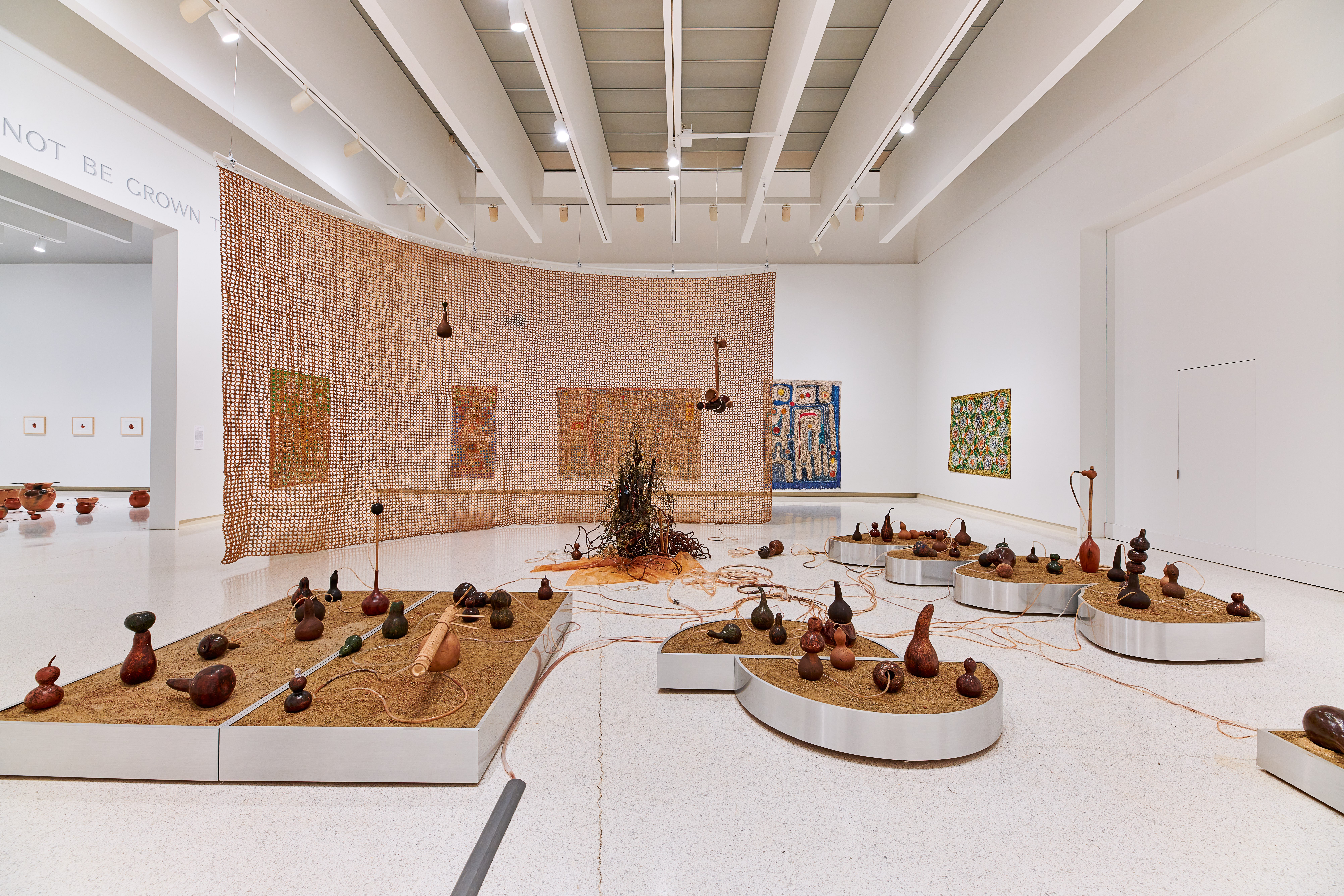A white wall gallery space that is densely filled with various floor standing sculptures and works hung on the walls.