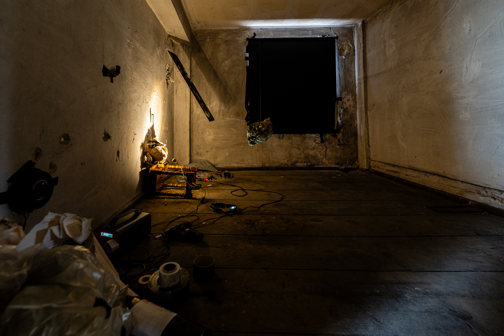 Bild 3 zu Fungillation: Niedriger abgedunkelter Raum, in dem an der linken Wand ein fu&szlig;ballgro&szlig;er runder Pilz lehnt, der von einer Lampe angeschienen wird. Dieser ist f&uuml;r Besuchende nur durch das Loch erkennbar. 