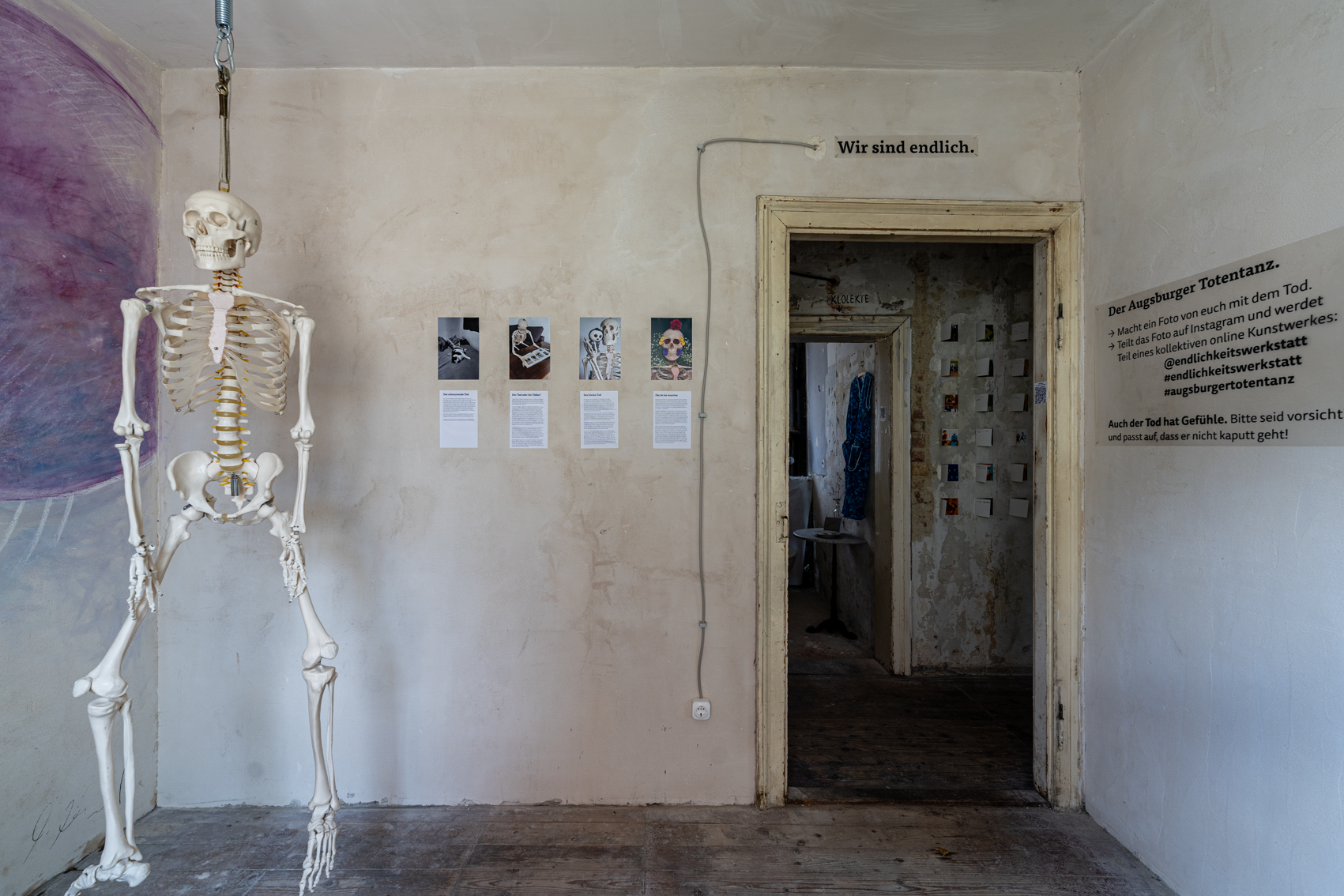 Bild 4 zu Augsburger Totentanz: Blick im Raum stehend auf den T&uuml;rrahmen. Links der T&uuml;r vier weitere Bilder, ganz links das Skelett. &Uuml;ber dem Ausgang steht: "Wir sind endlich".