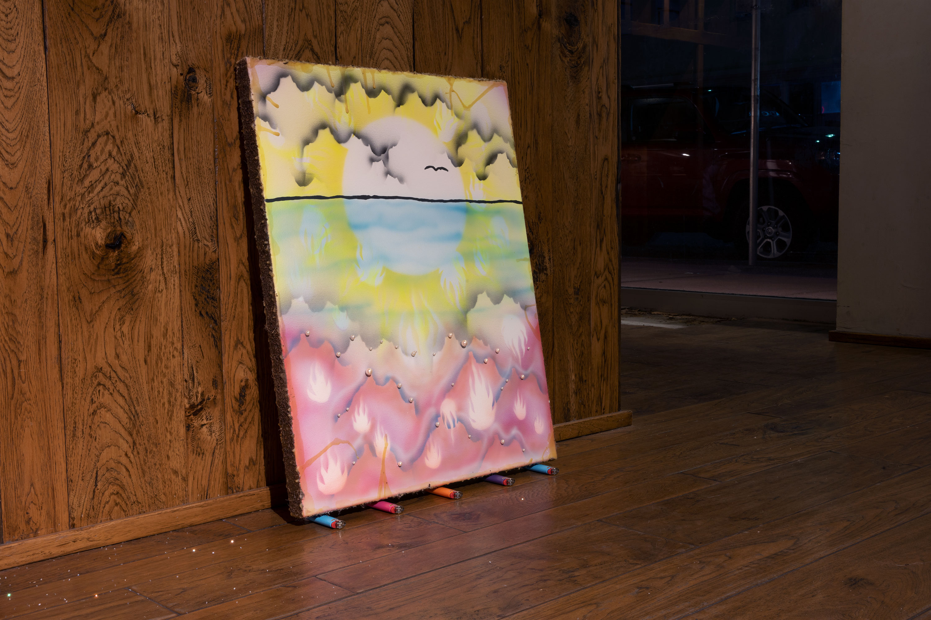 Orlando Estrada, The Infinite Vision in the Ethereal Rainbows Swarming Behind my Eyelids Reveals a Beacon, 2021, coconut fiber, beeswax, artificial pearls, cigarette lighters, acrylic on canvas, 31” x 24”. A black line separates a yellow and blue sky as rigid forms filled with white bundles of flames create an almost mountainous purple and pink landscape in the foreground; five colored lighters act as the base for the canvas.