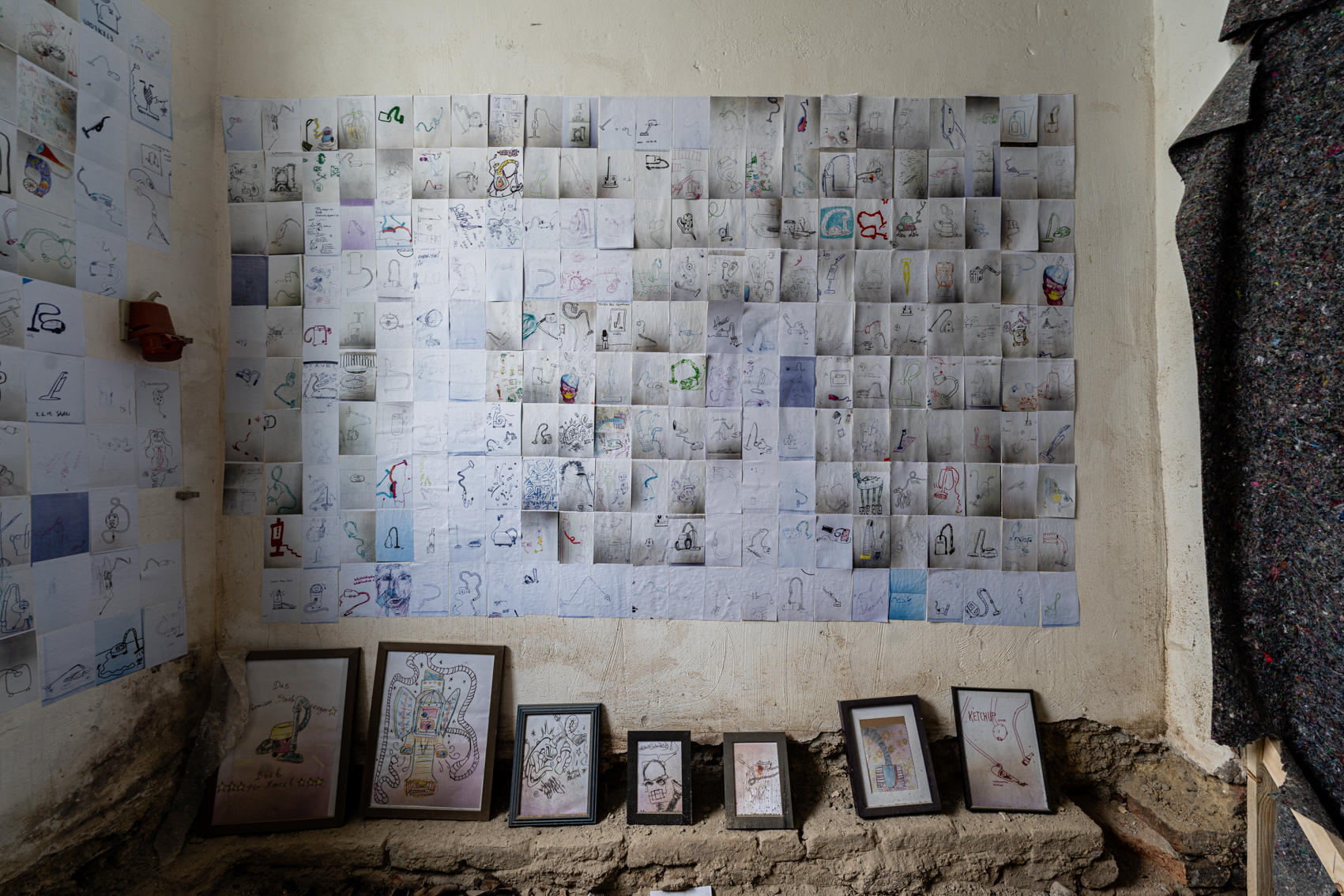 Bild 3 Staubsauber: Die rechte Wand ist ebenfalls voller Zeichnungen von Staubsaugern. Auf dem sandigen Boden stehen eingerahmte gr&ouml;&szlig;ere Zeichnungen.