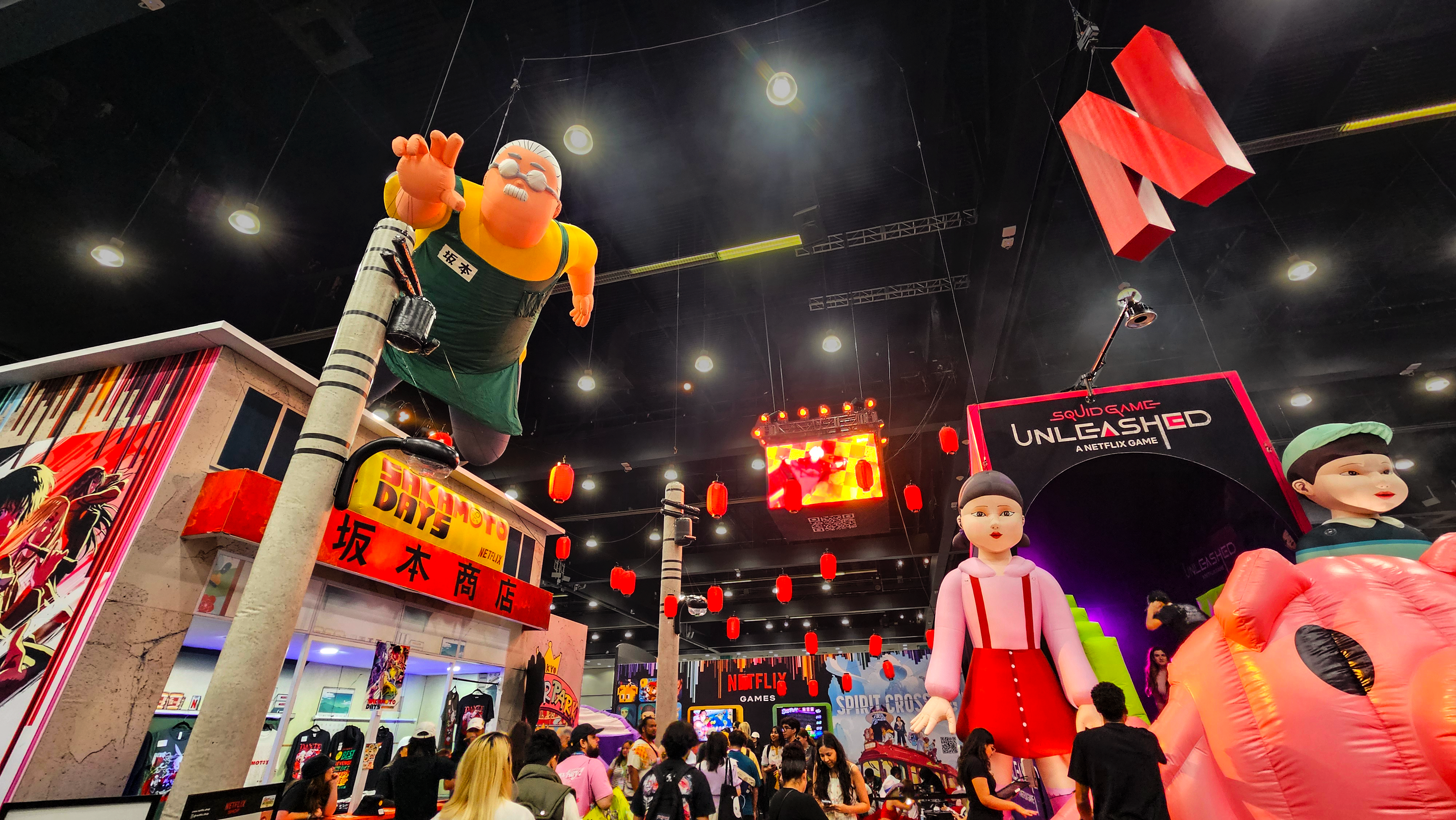 AERIAL VIEW: Red lanterns and telephone polls completed the Sakamoto Days "street". For an even more dynamic skyline, we added a giant floating Mr. Sakamoto, jumbotron, and Netflix N to fully populate the air and act as a beacon to the rest of the hall.