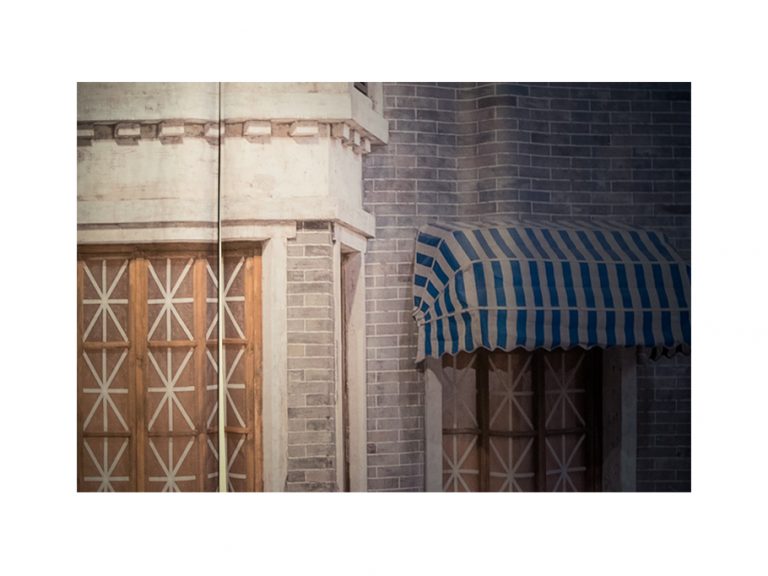 A close up of printed photograph of a building facade juts out from the right wall as a 3D wall installation in the gallery.