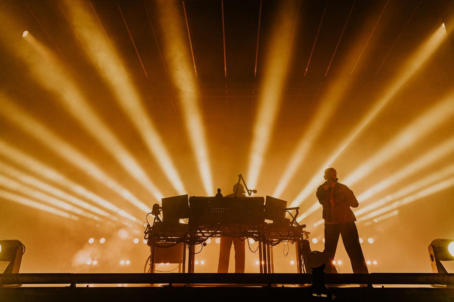 Underworld live at AVA Festival 2025 with golden stage lights radiating outward in BelfastUnderworld live at AVA Festival 2025 with golden stage lights radiating outward in Belfast