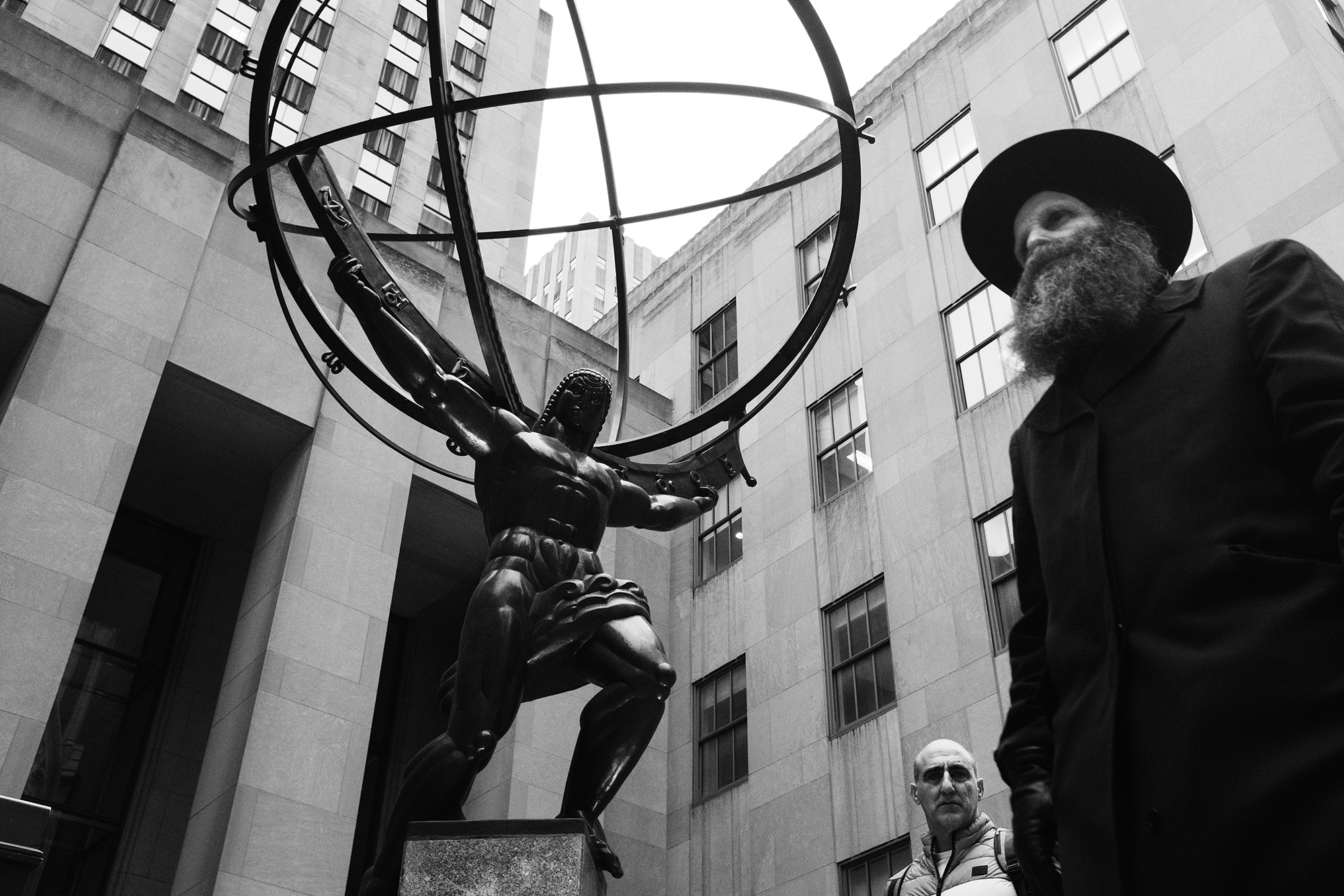 Philippe-Sarfati-early-work-photography-photographer-street-documentary-black-and-white-rockefeller-center-new-york-city-nyc-usa-religious-man-black-hat-coat-walking-atlas-world-shoulders-art-deco-statue-responsibility-sphere