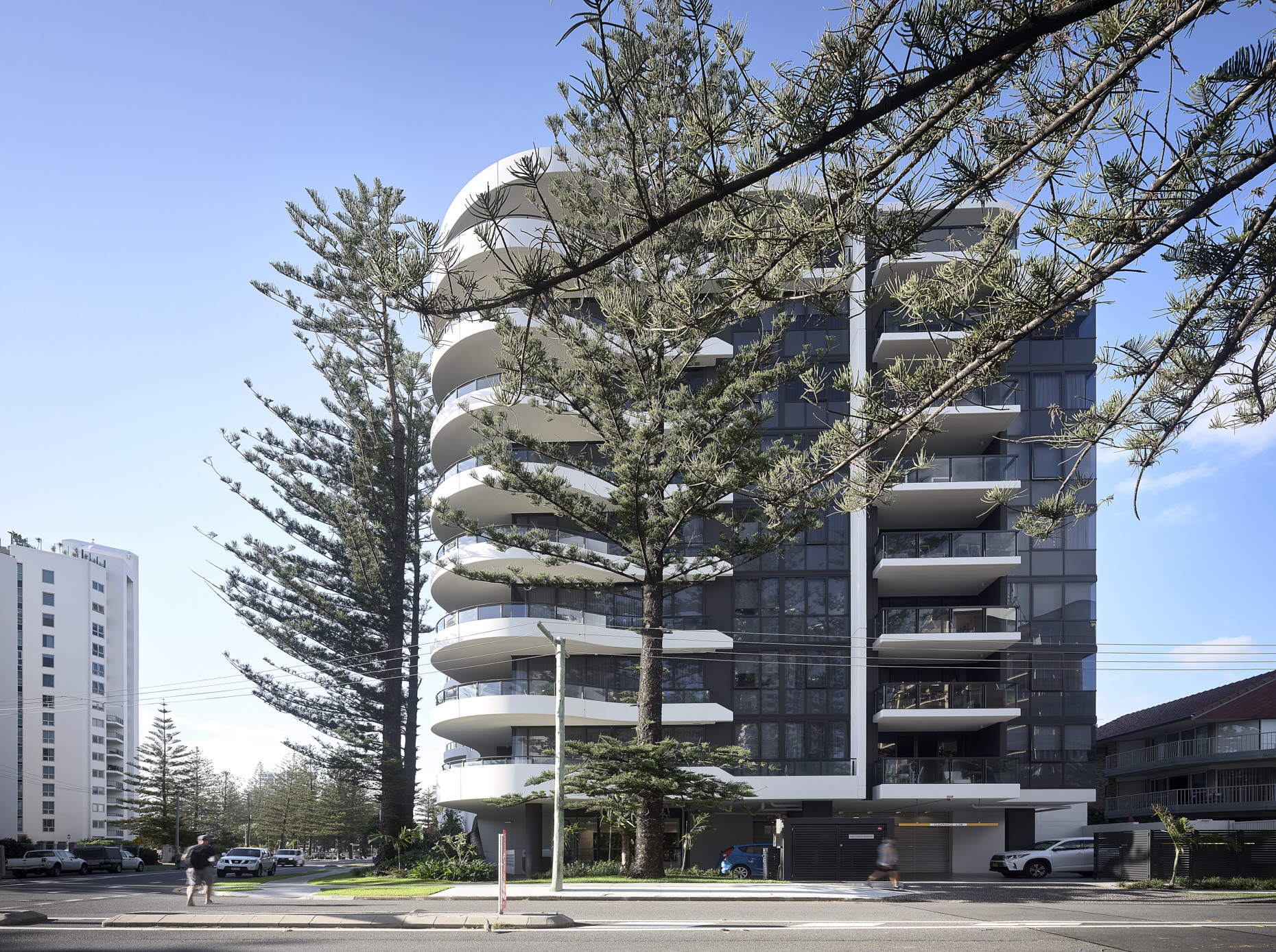 A contemporary apartment building with a curved façade and dark recesses and tinted glazing.