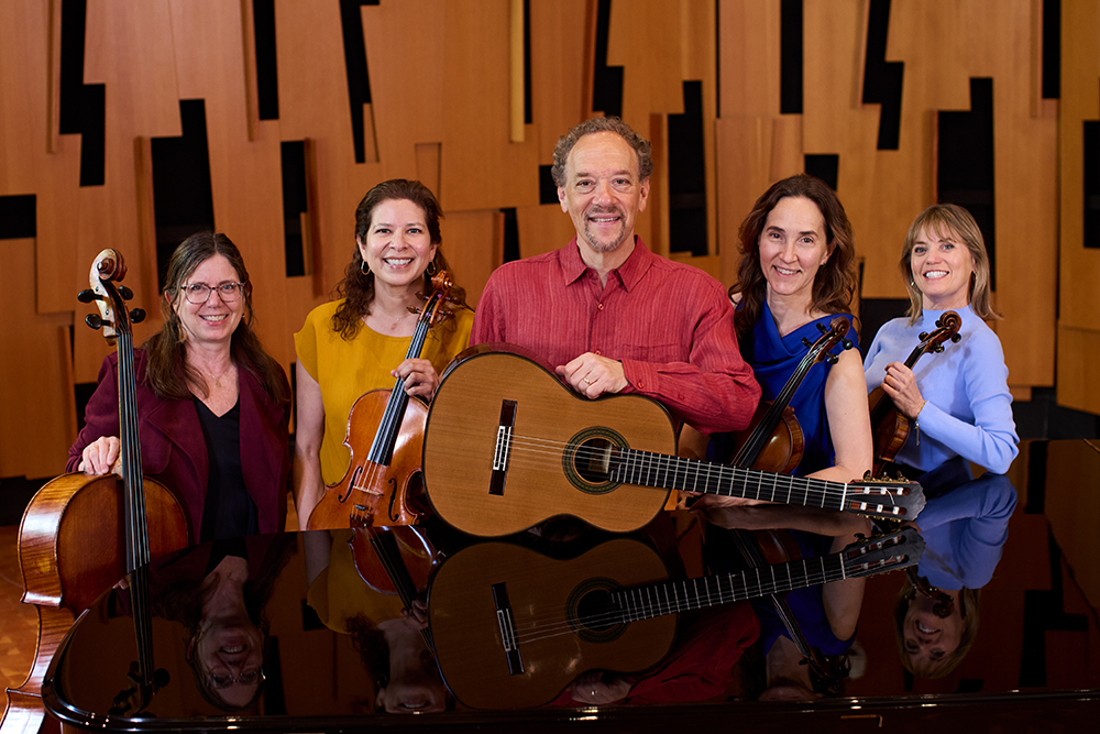 A group of five musicians are each holding their instrument and smiling.