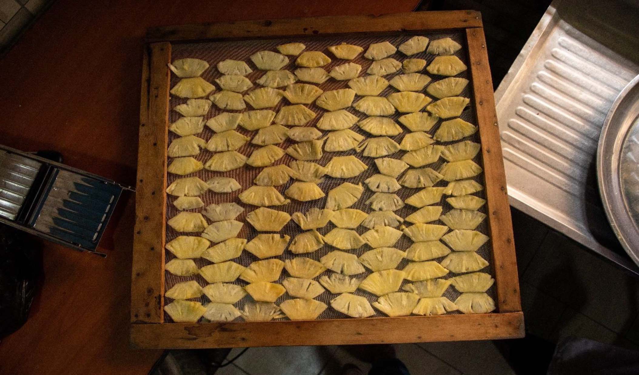 Des tranches fines d'ananas frais, disposées en rangées sur la grille de séchage. Faridah a d'abord utilisé un petit séchoir solaire Sun Oven, puis un plus grand séchoir à charbon Sparky.