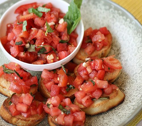 seen from above, a bowl of colorful diced tomatoes surrounded with tasty prepared bruschetta