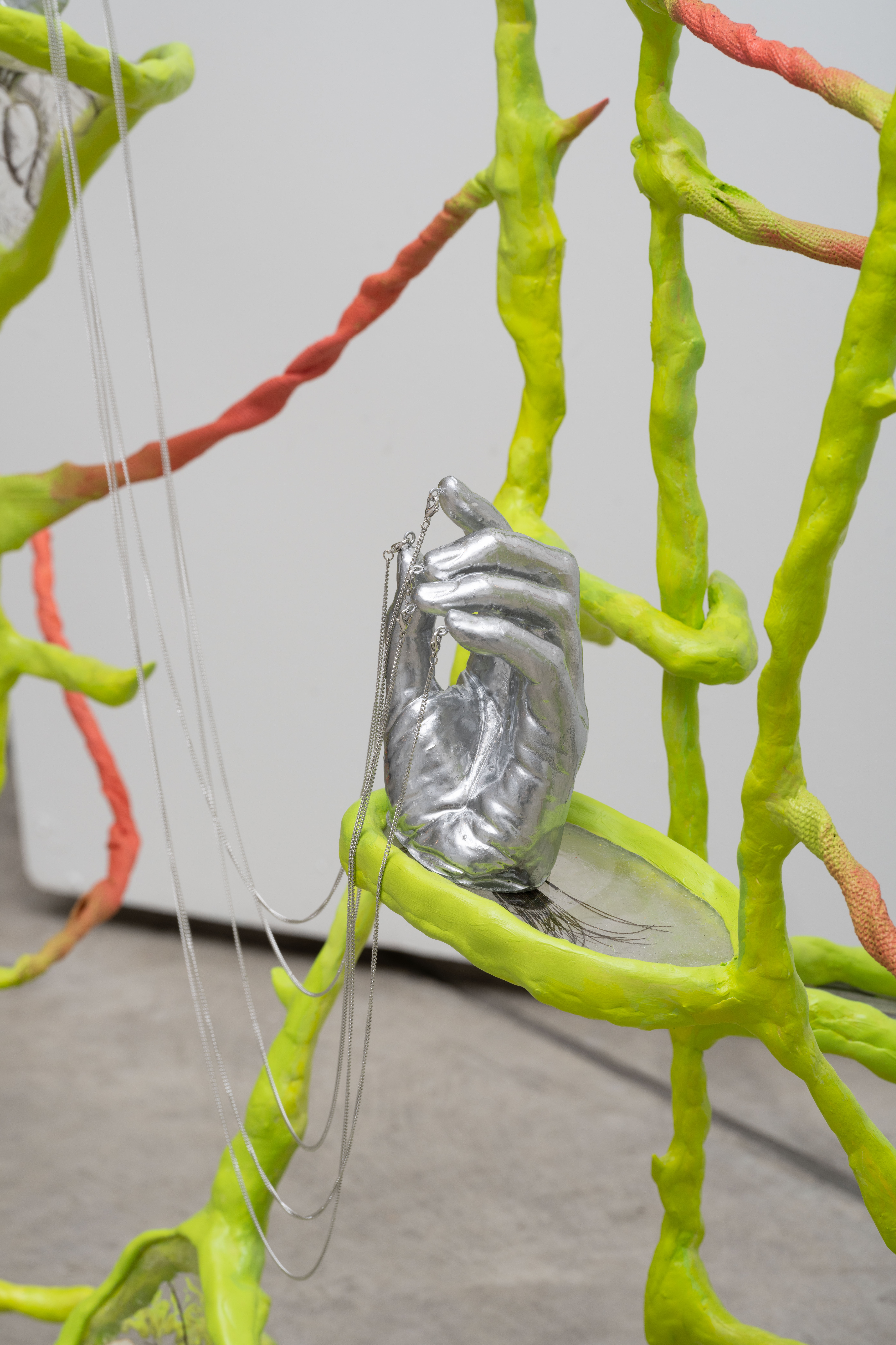 detail of remedies, 2023. Epoxy clay, resin, peacock feathers, medical casting tape, DuoMatrix, necklace chains, and half empty sake bottle. 48” x 203” x 24”