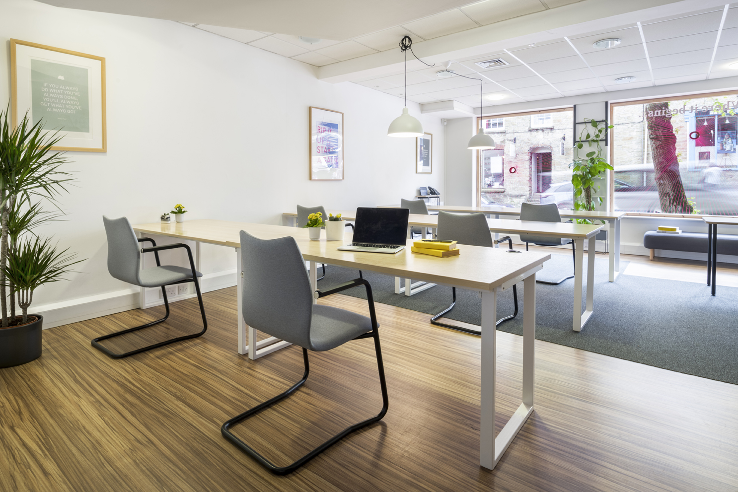 Modern office with neutral desks and grey chairs. Timber flooring with grey carpeted area. White walls and ceiling.