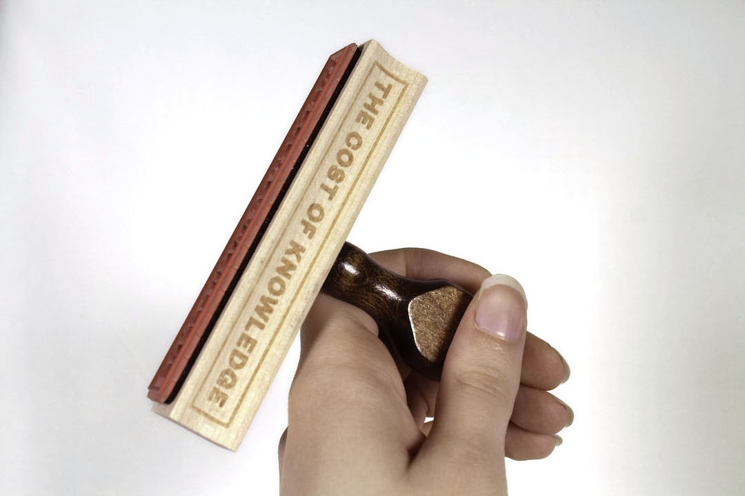 Physical stamp for "The Cost of Knowledge" logo