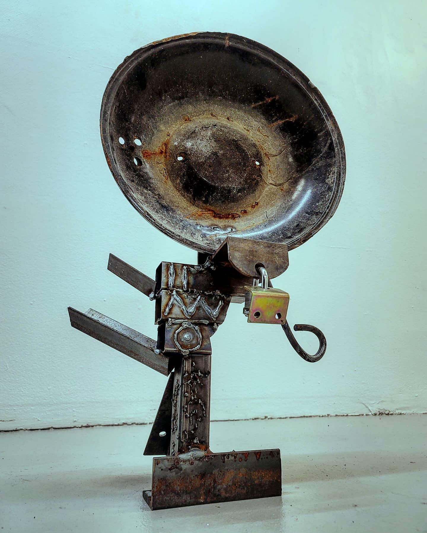 A floor standing sculpture of welded together pieces of stock steel that resembles a small satellite dish for some unknown purpose.