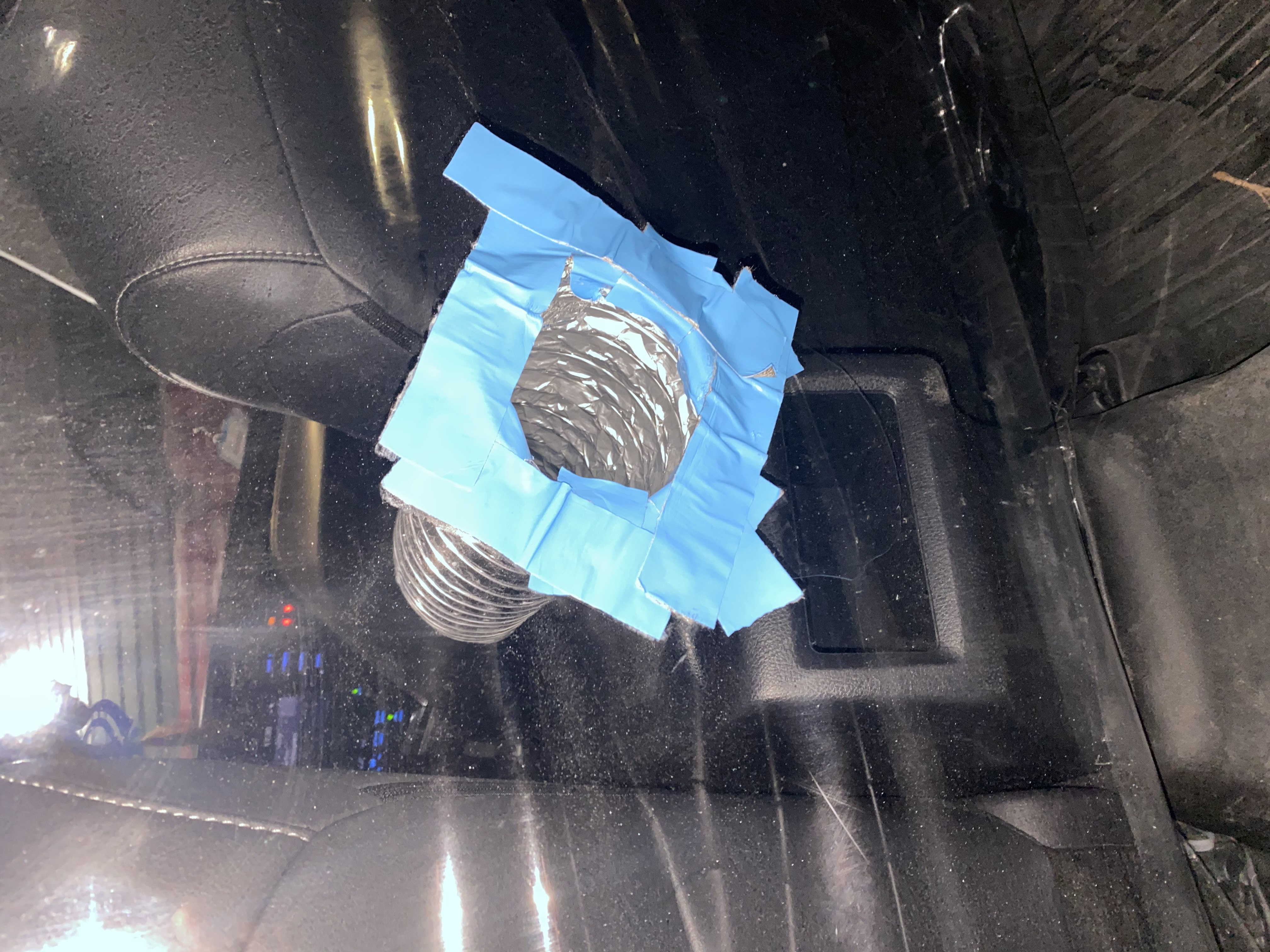 Flash photograph from the backseat of a car with a piece of plastic separating the driver/passenger seat from the back. A duct taped silver tube through the plastic.