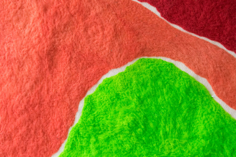 Pictured: A close up of one square piece of hand dyed wool with red, orange and green sections. The texture of the wool is visible.