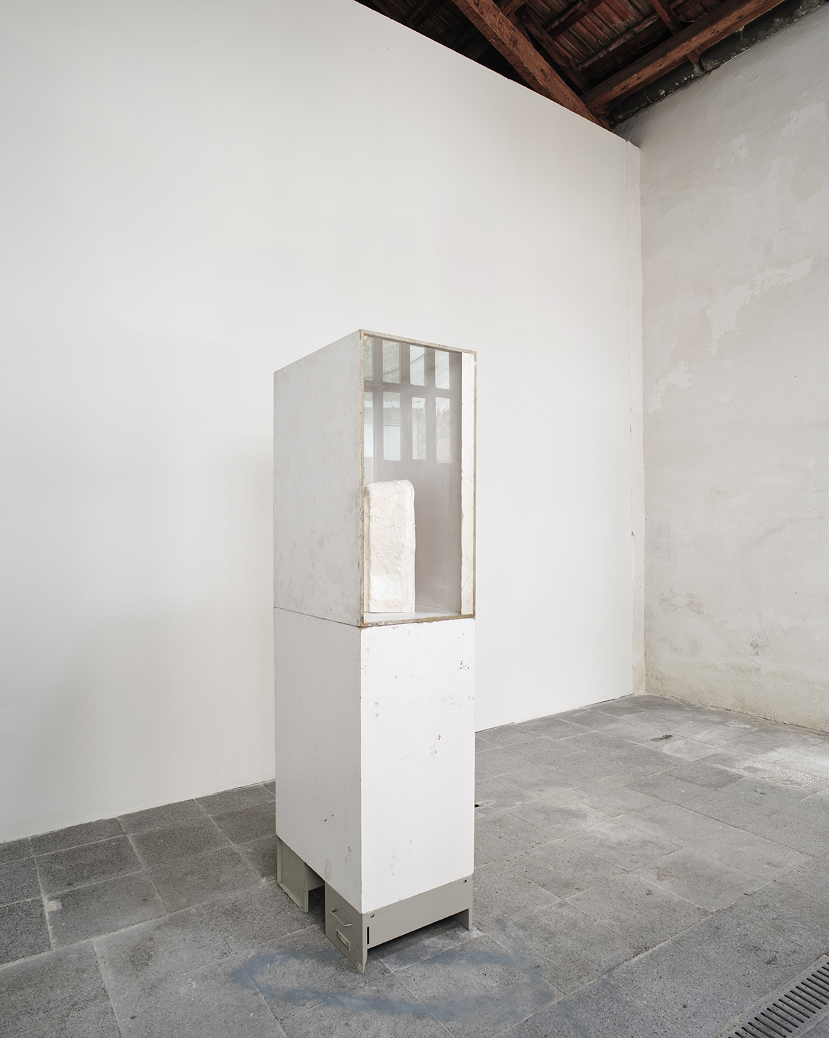 You who are the stranger (Torso), 2022. Marks of use on found wooden plinths, remnants of the acrylic resin mould of the Opel Olympia sculpture made in collaboration between the artist and his father, plaster strips, inkjet print on Epson photographic paper glued on wood, museum glass, found metal filing cabinets. 178 x 60 x 40 cm.