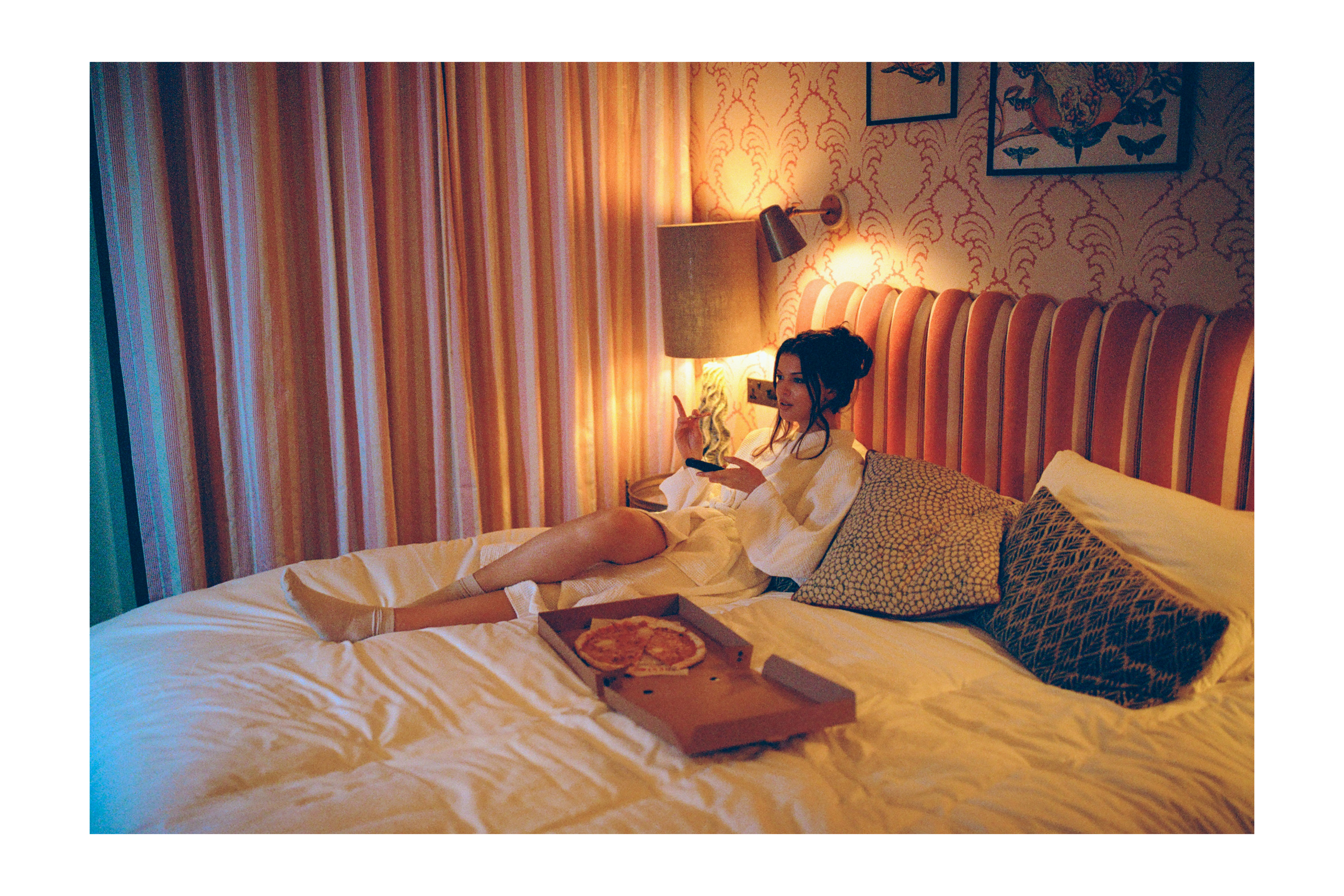 Film photo of model in bed eating pizza in hotel photographed by Dublin based lifestyle, fashion, and advertising photographer Alex Sheridan