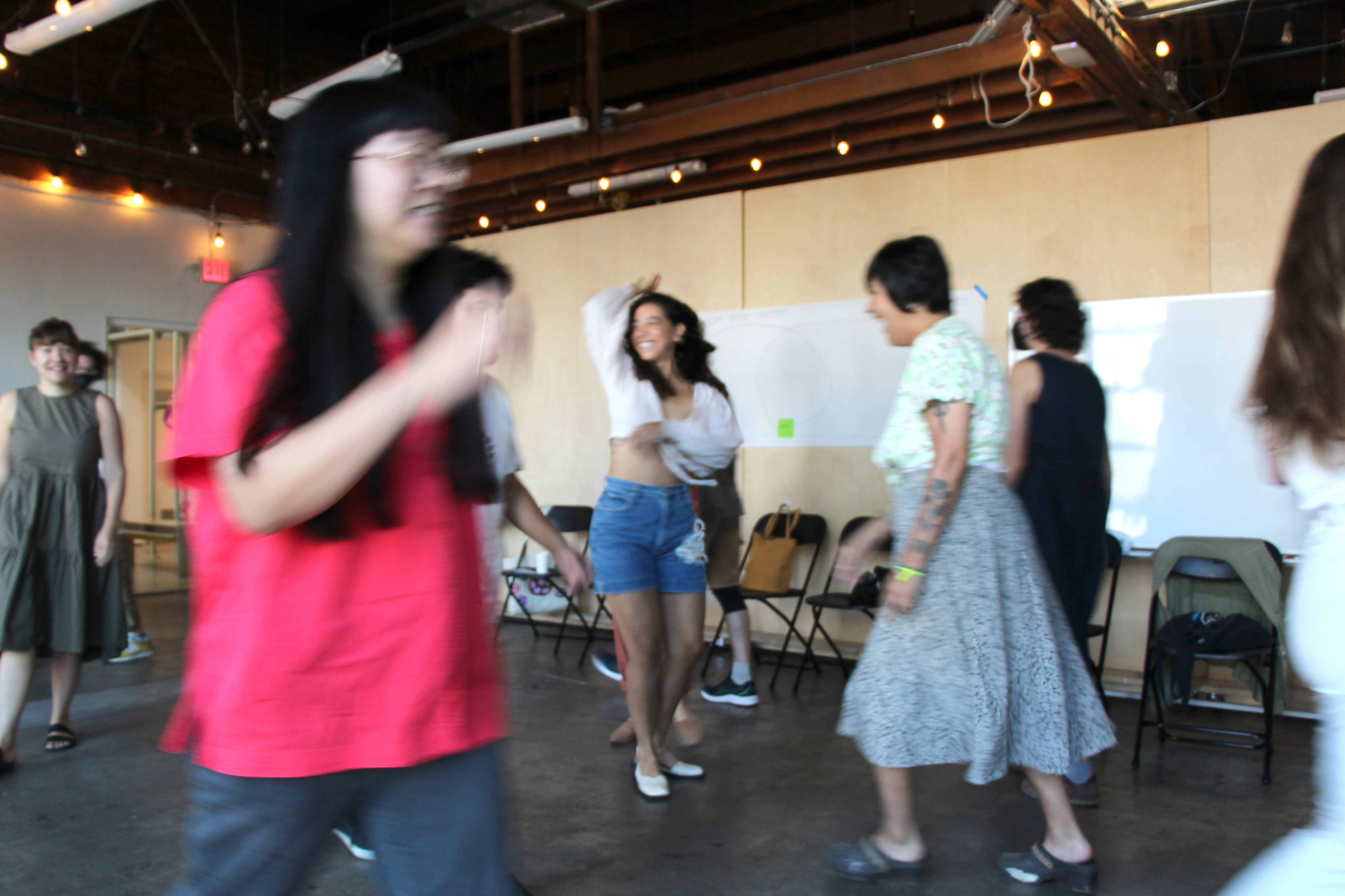 Adults joyfully move around a workshop space in front of a line of chairs.