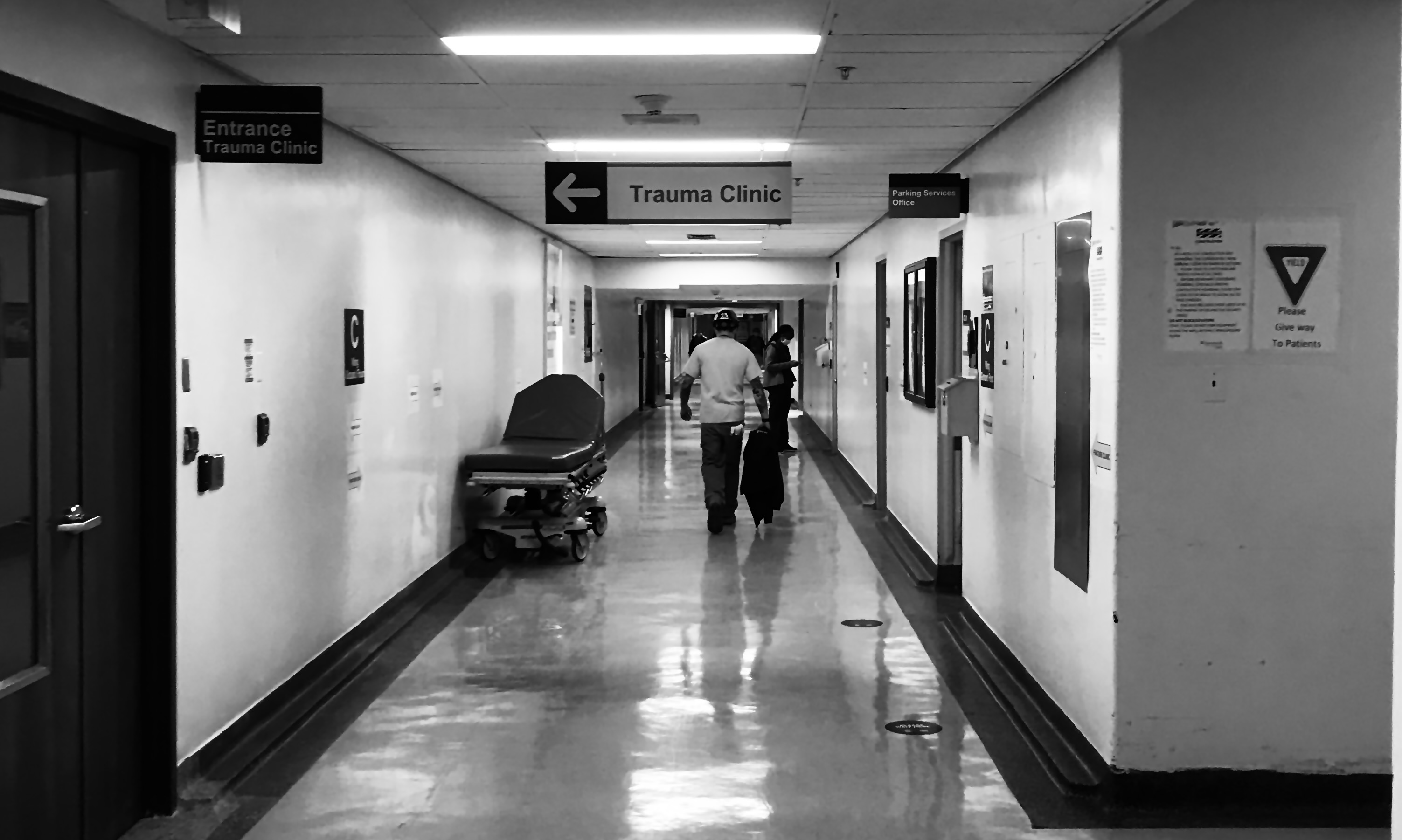 A male figure walks down a long white hospital hallway. A wayfinding sign reads: Trauma Clinic.