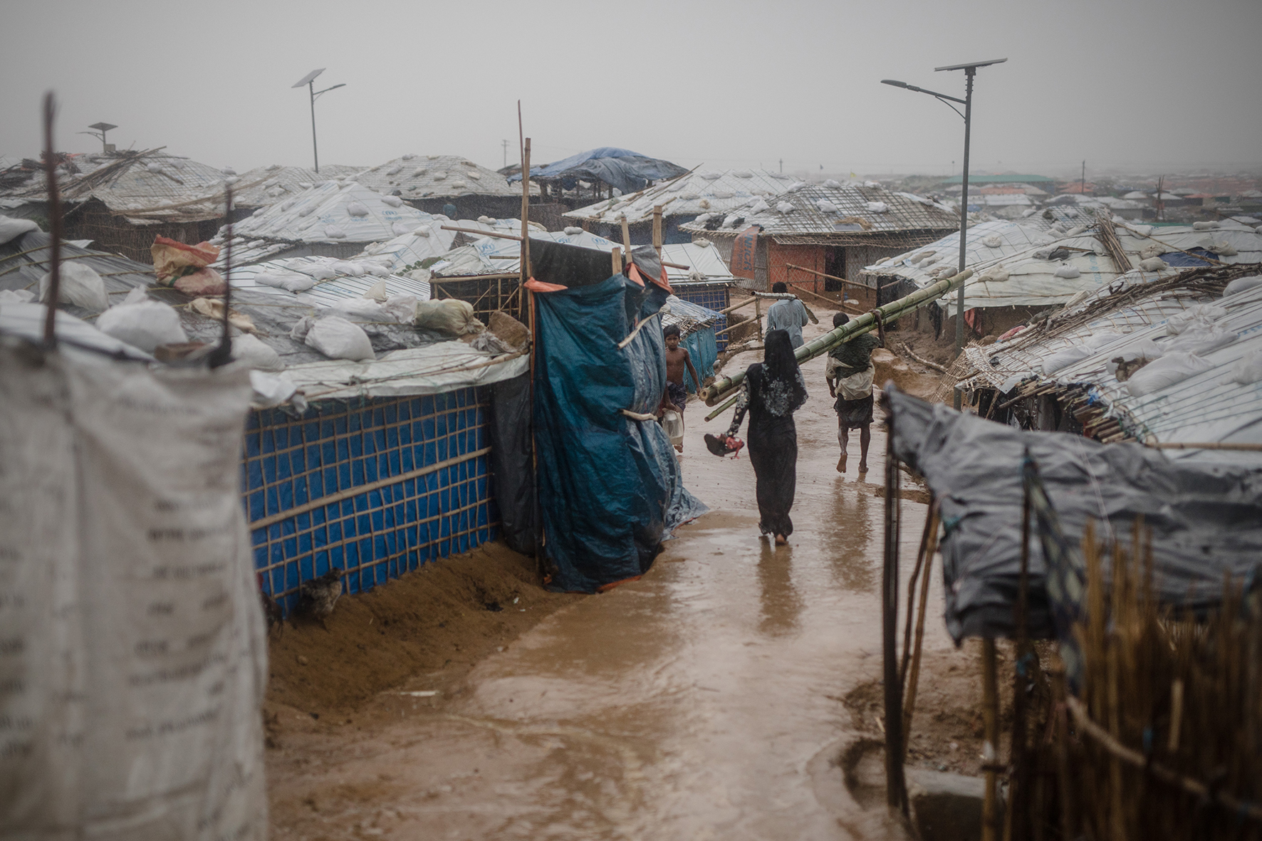 Residents of Kutupalong camp making their way through a sudden rainstorm. Rain makes the pathways very slippery, often causing people to fall and injure themselves. It also increases the likelihood of landslides.