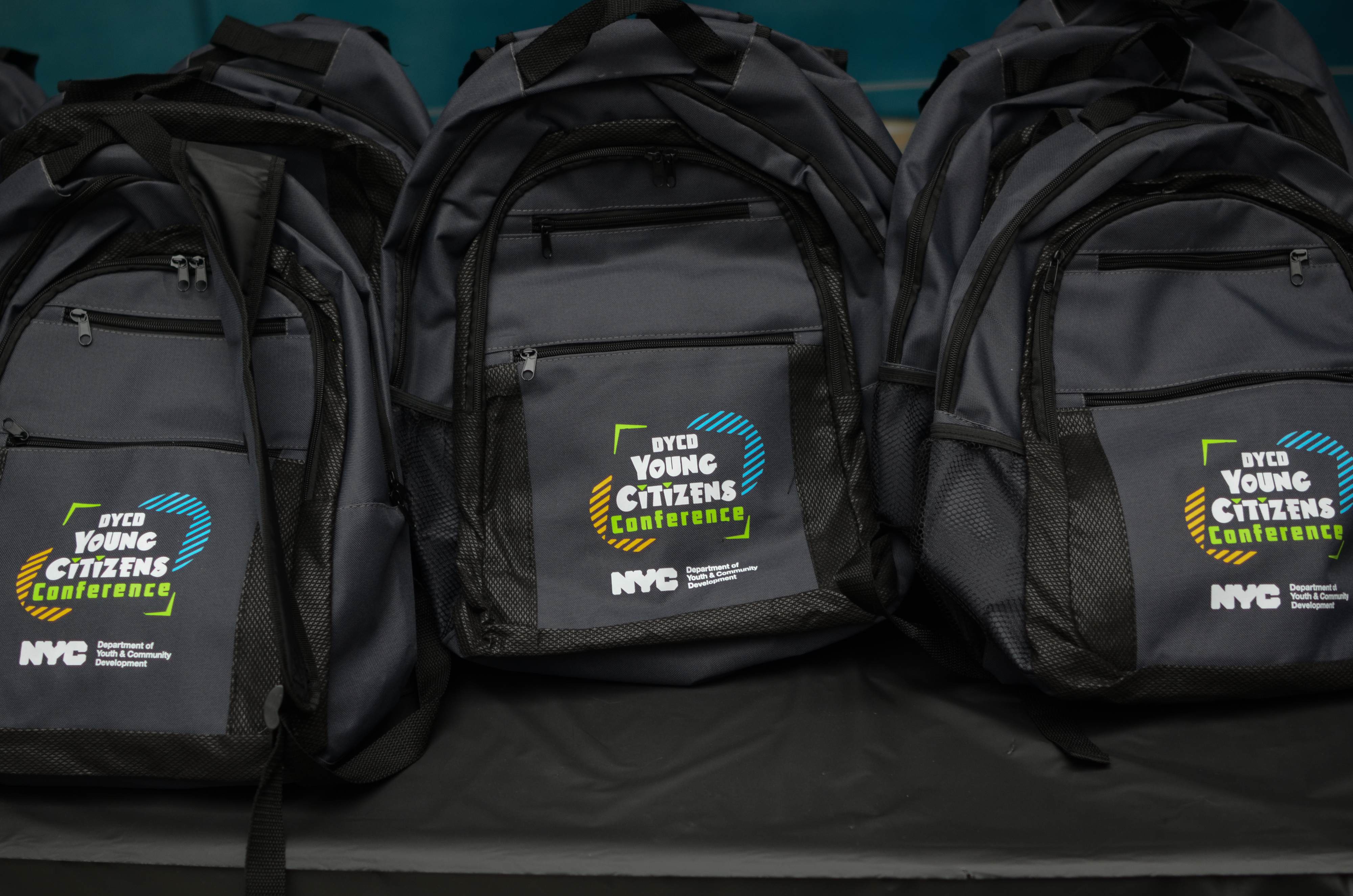 Several black backpacks with the DYCD Young Citizens Conference full color logo printed on the front pocket.