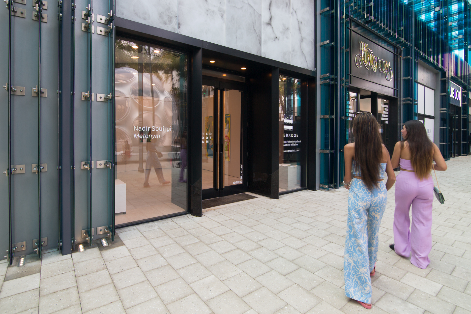 Nadir Sourgi, Installation view of Metonym at Bas Fisher Invitational as part of Waterproof Miami, Photo by Monica McGivern (2022). Two people on the right viewing the outside facade of the gallery space.