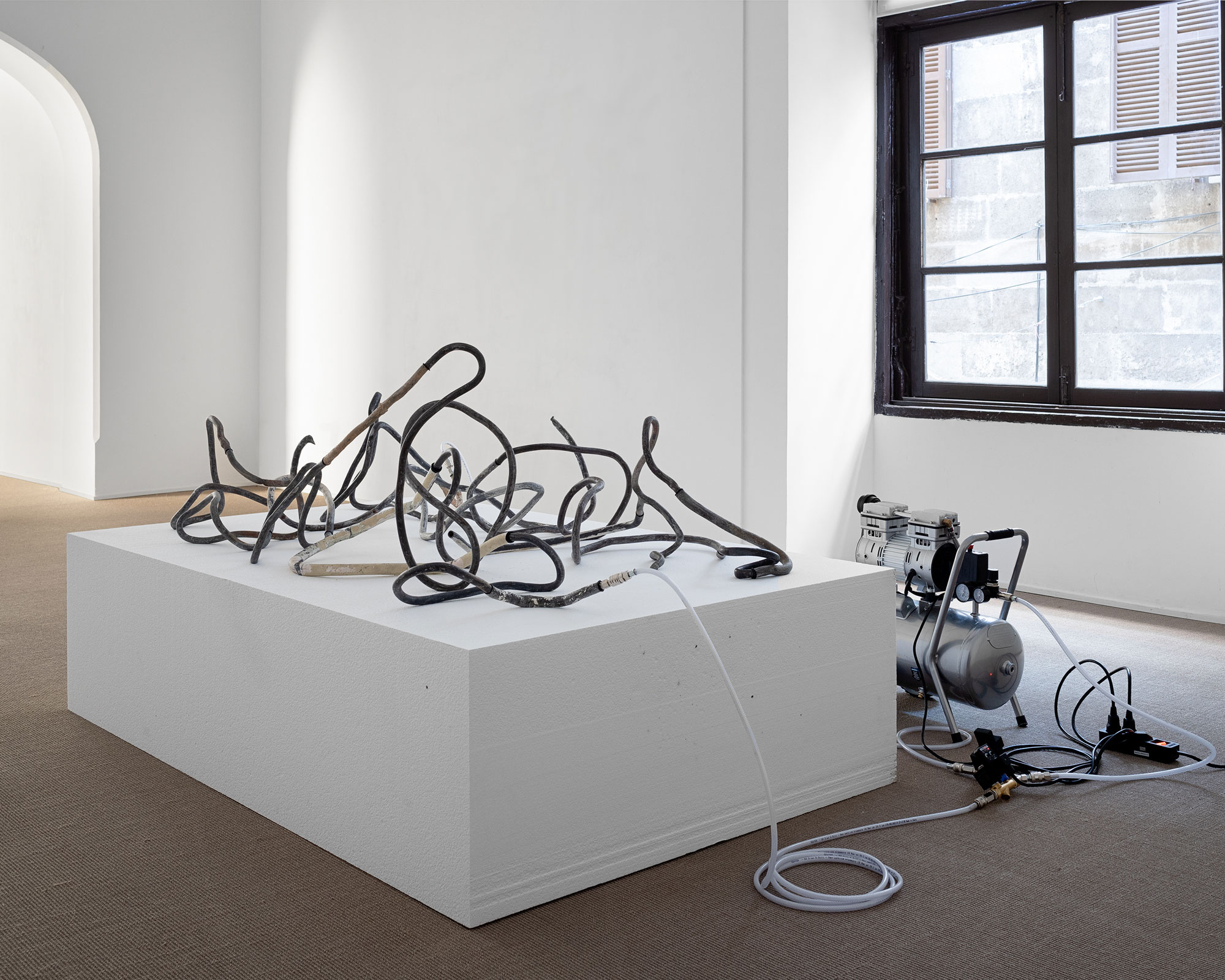 Mallorca 69 (Lead Thread #5), 2025Fragments of lead pipes, pigeon feathers, aluminum tube, MS polymer, rubber O-rings, air compressor, plastic and steel pneumatic components, timed valve, expanded polystyrene, wiring.200 × 185 × 100 cm.Installation view at Processionària,  Galeria Pelaires, Palma, 2024Photo: Juan David Cortés