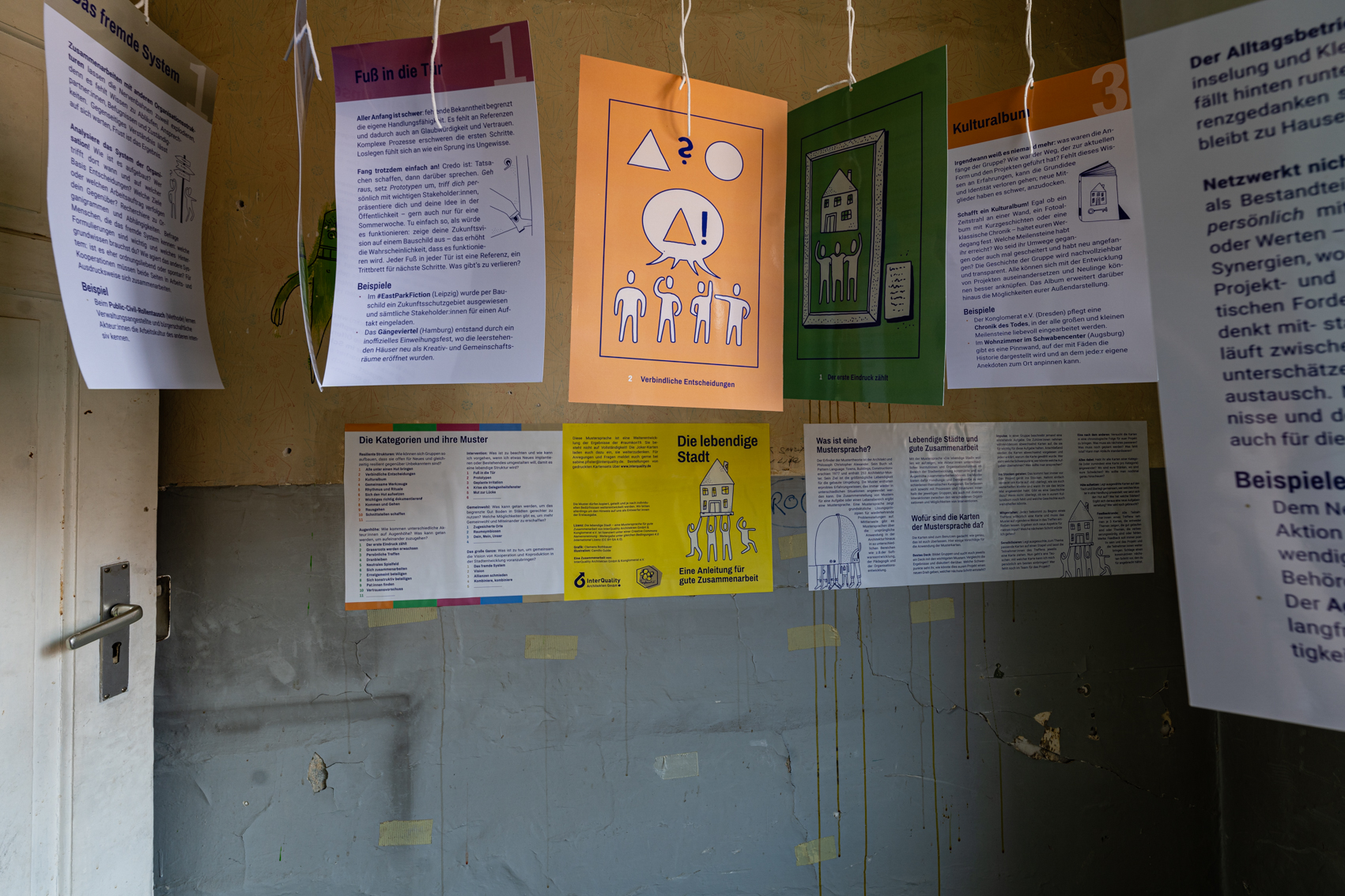Bild 2 zu Musterk&uuml;che: N&auml;here Ansicht der Karten, die an F&auml;den h&auml;ngen. An der Wand im Hintergrund h&auml;ngen ebenfalls Informationen zu dem Projekt "Die lebendige Stadt".