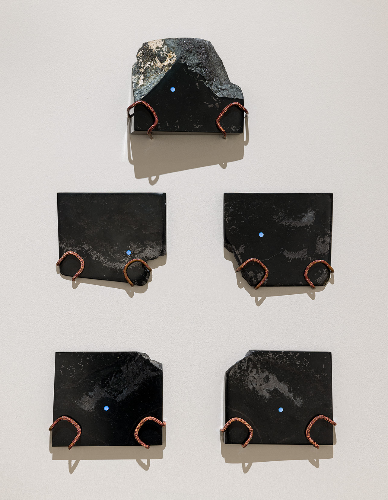 Joel Kuennen, "A Messianic Frame I-V," 2023. Fine-grain basalt with nickel and iron inclusions (California), labgrown olivine (EPFL, Switzerland), strontium aluminate europium dysprosium, UV resin, copper, beeswax, 15 x 21 x 2 1/2 inches. Photo by Etienne Frossard. 