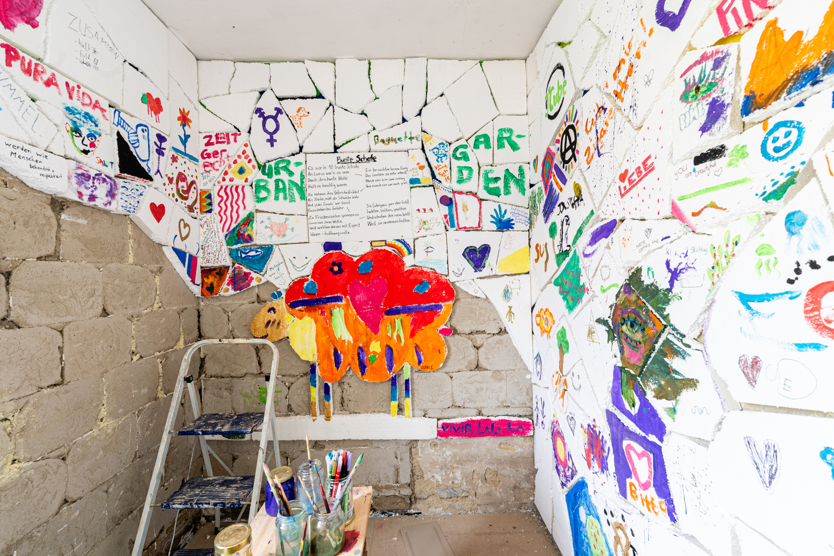 Bild 3: Zwischen schwarz und wei&szlig;: N&auml;here Ansicht der bemalten Styroporfl&auml;che. Ein rot, gelb orange bemaltes Schaf aus Styropor ist auf der gegen&uuml;berliegenden Wand abgebildet.