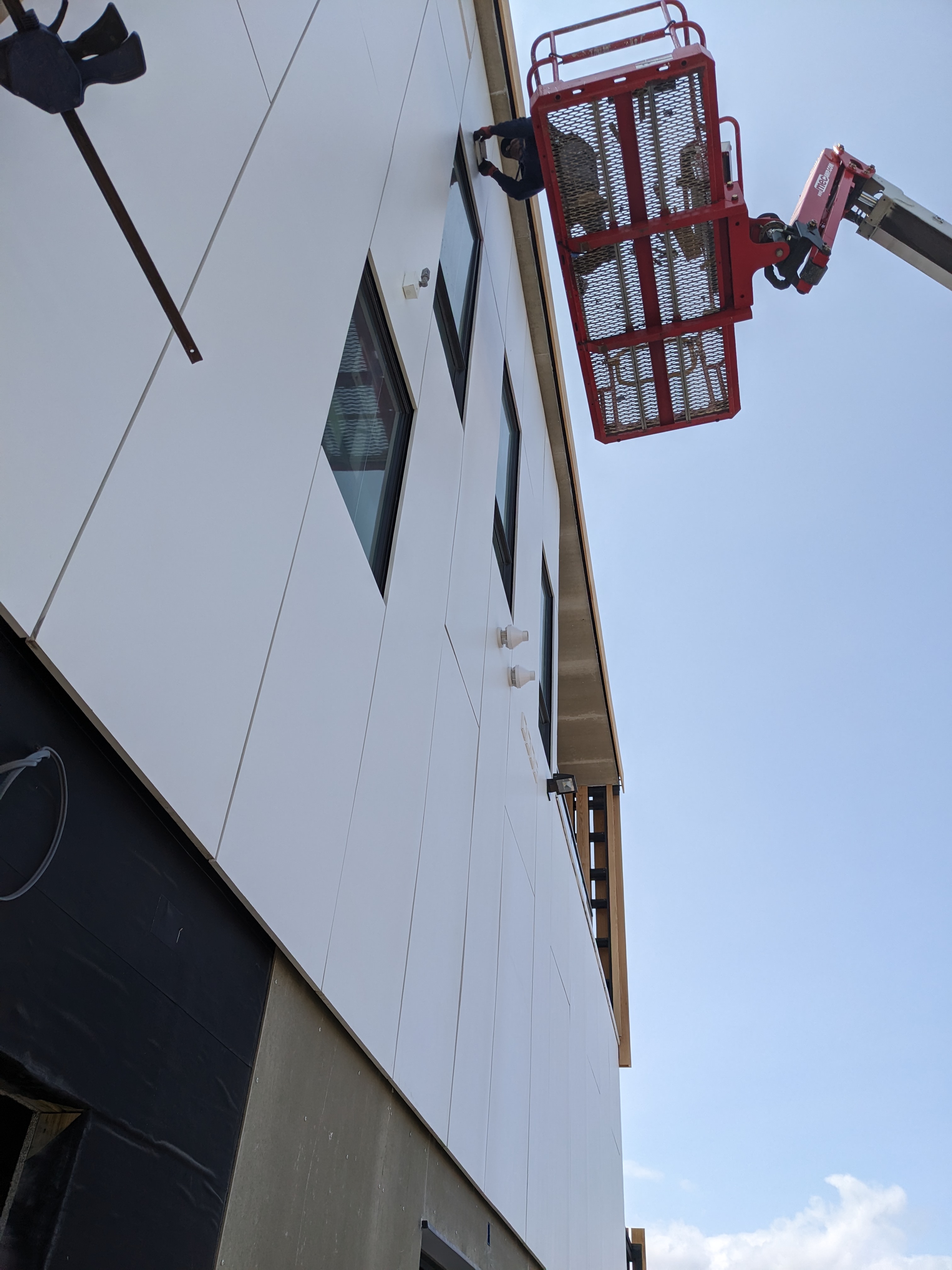 Close-up construction photo of the Brigantine Marina Paddle Club exterior, showing the installation of the crisp white panel cladding from a lift.