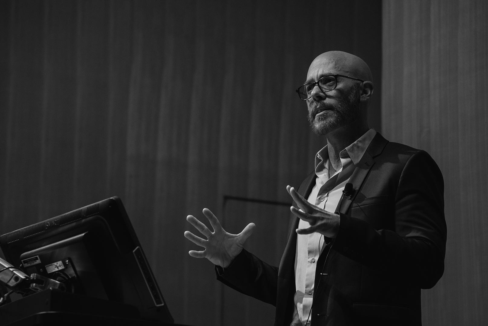 Stephen Phillips, Man wearing glasses and a formal jacket standing in front of a computer screen gesticulating and giving a presentation.