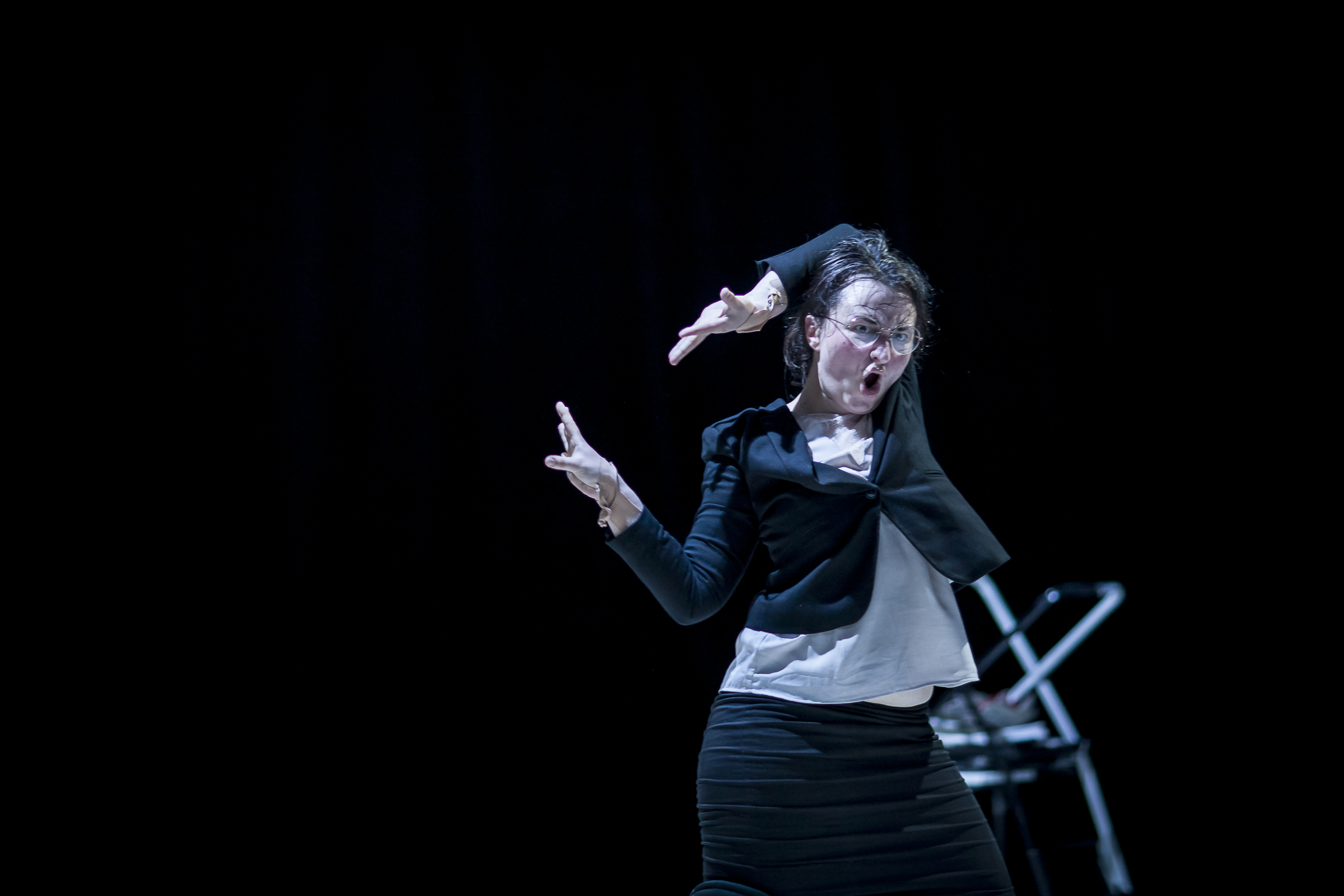 Image 8 of 10: A woman in a black skirt suit dancing awkwardly