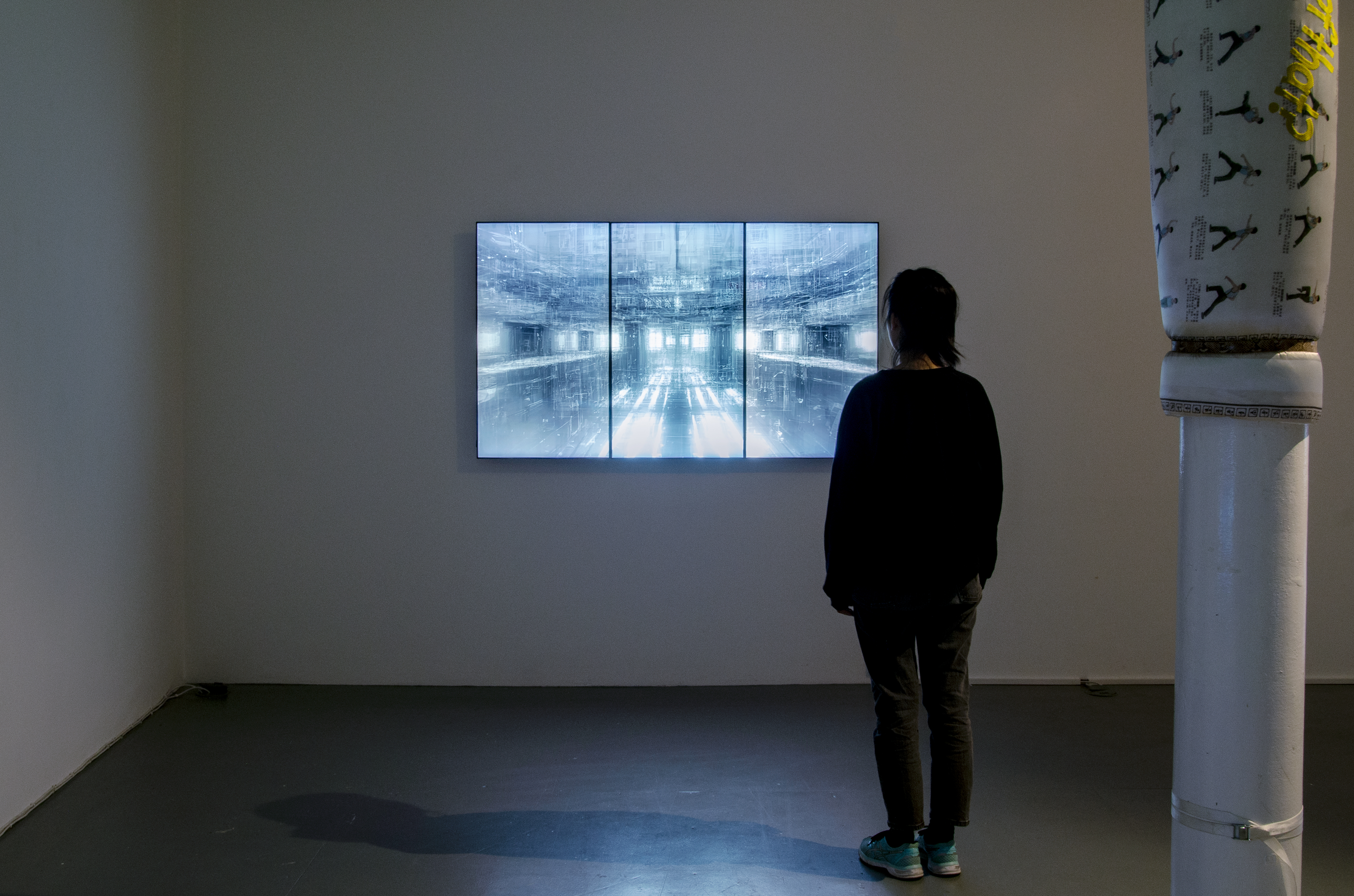 Inside the gallery, a person stands to right, in front three connected screens. They face the screens.