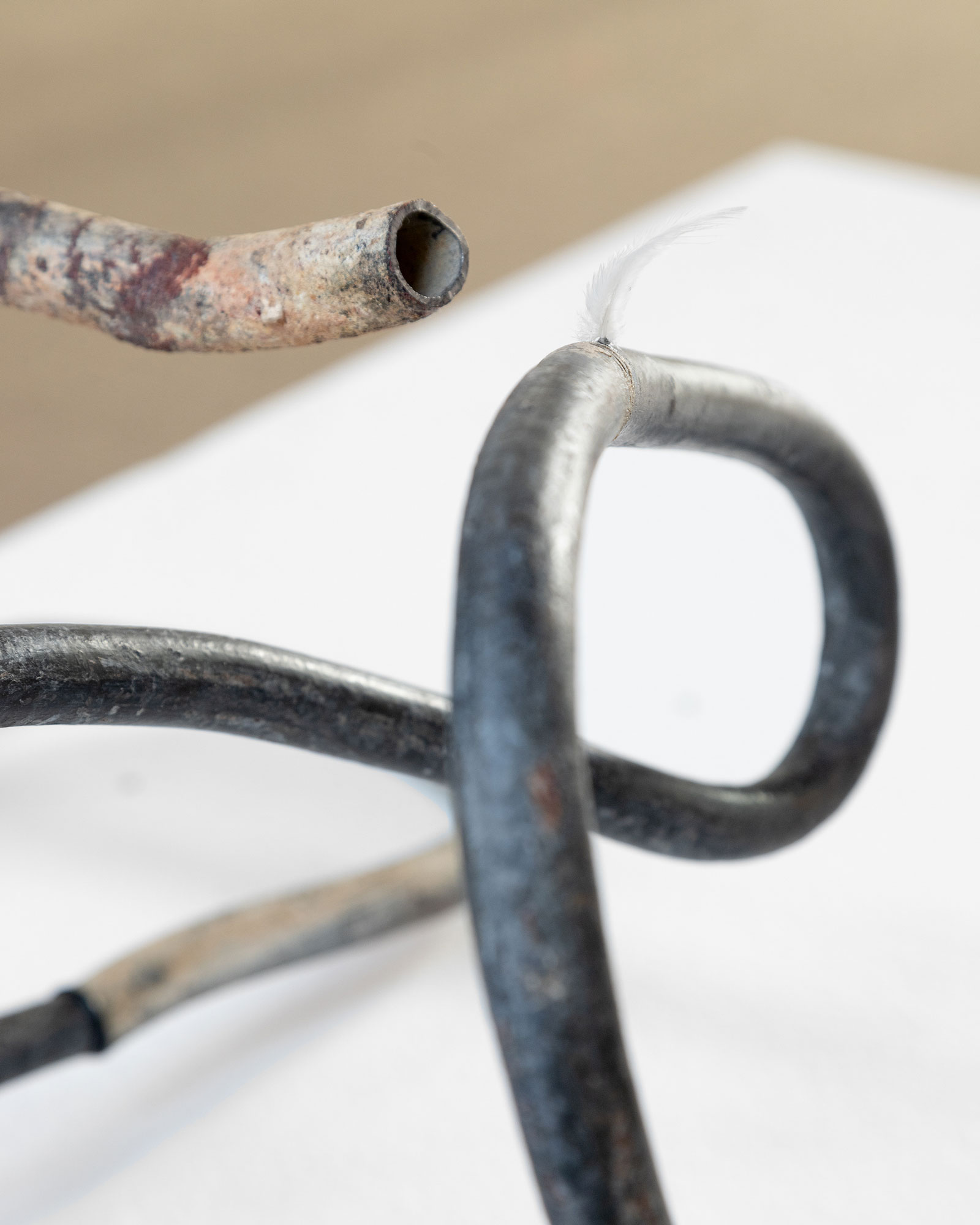 Mallorca I (Lead Thread #4), 2024 [detail]Fragments of lead pipes, pigeon feather, aluminum tube, MS polymer, rubber O-rings, air compressor, plastic and steel pneumatic components, timed valve, expanded polystyrene, wiring.270 × 115 × 100 cm.Installation view at Processionària, Galeria Pelaires, Palma, 2024Photo: Juan David Cortés