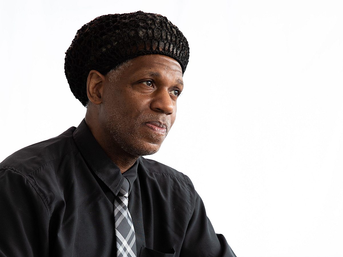 Portrait of a smiling staff member in a black hat, black shirt, and argyle tie.