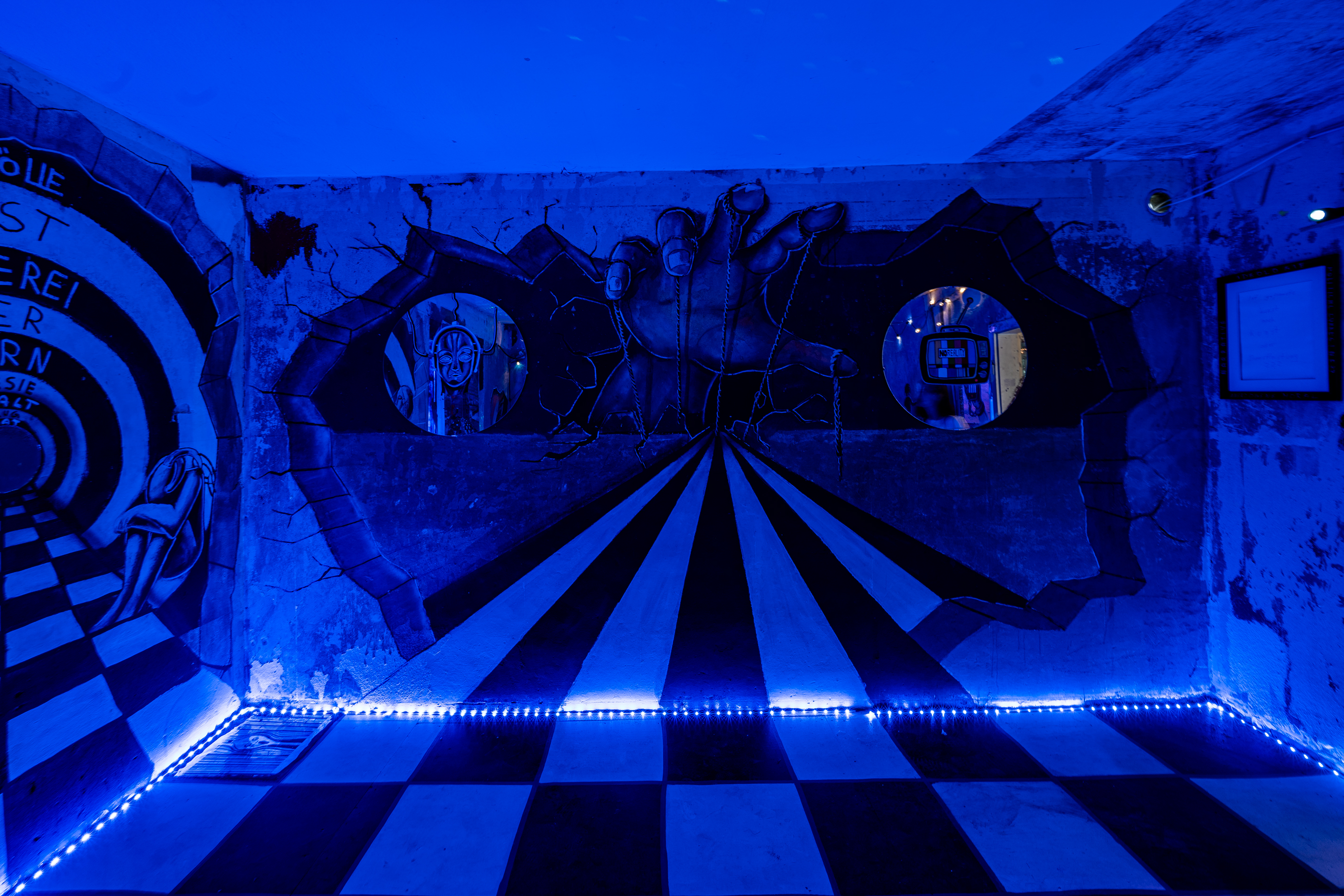 Bild 4 Eyes Wide Shut: Die rechte Wand des Raumes. Das Schachbrettmuster verl&auml;uft spitz zusammen und wird von einer realistisch gemalten Hand mit F&auml;den nach oben gezogen. 