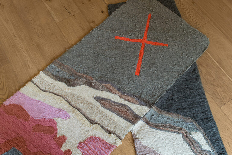 Pictured: Wool rug with vague landscapes on one side and an orange x with a grey background on the other side.