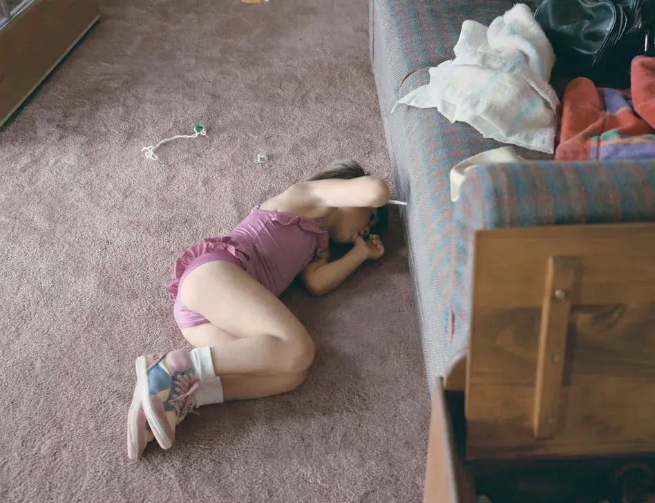 Little girl in a pink leotard with her thumb in her mouth as she lays on the floor. 