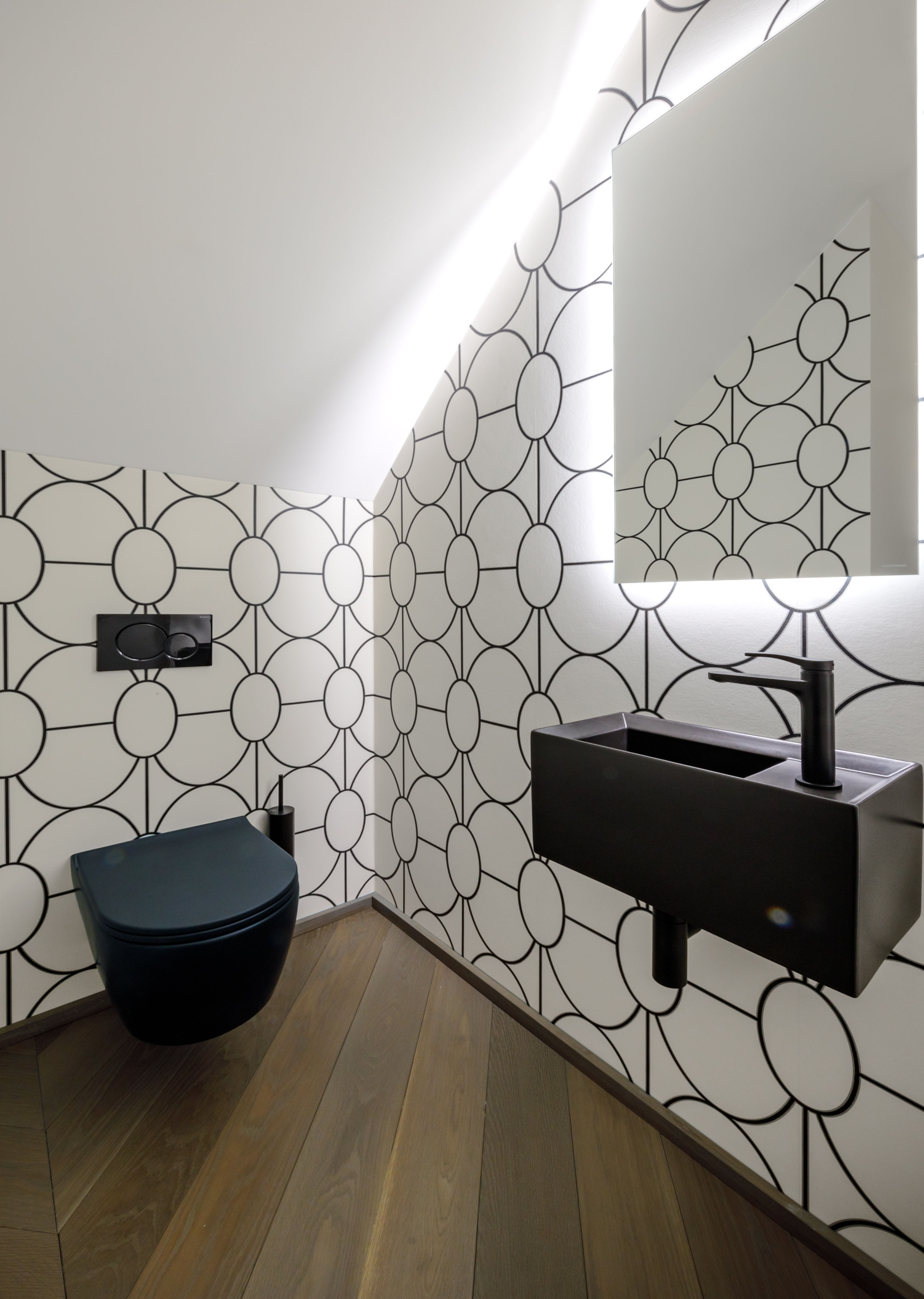 In der Gästetoilette reflektiert der Spiegel die grafische Tapete. Auch die Armaturen und Badmöbel sind ganz in schwarz gehalten.